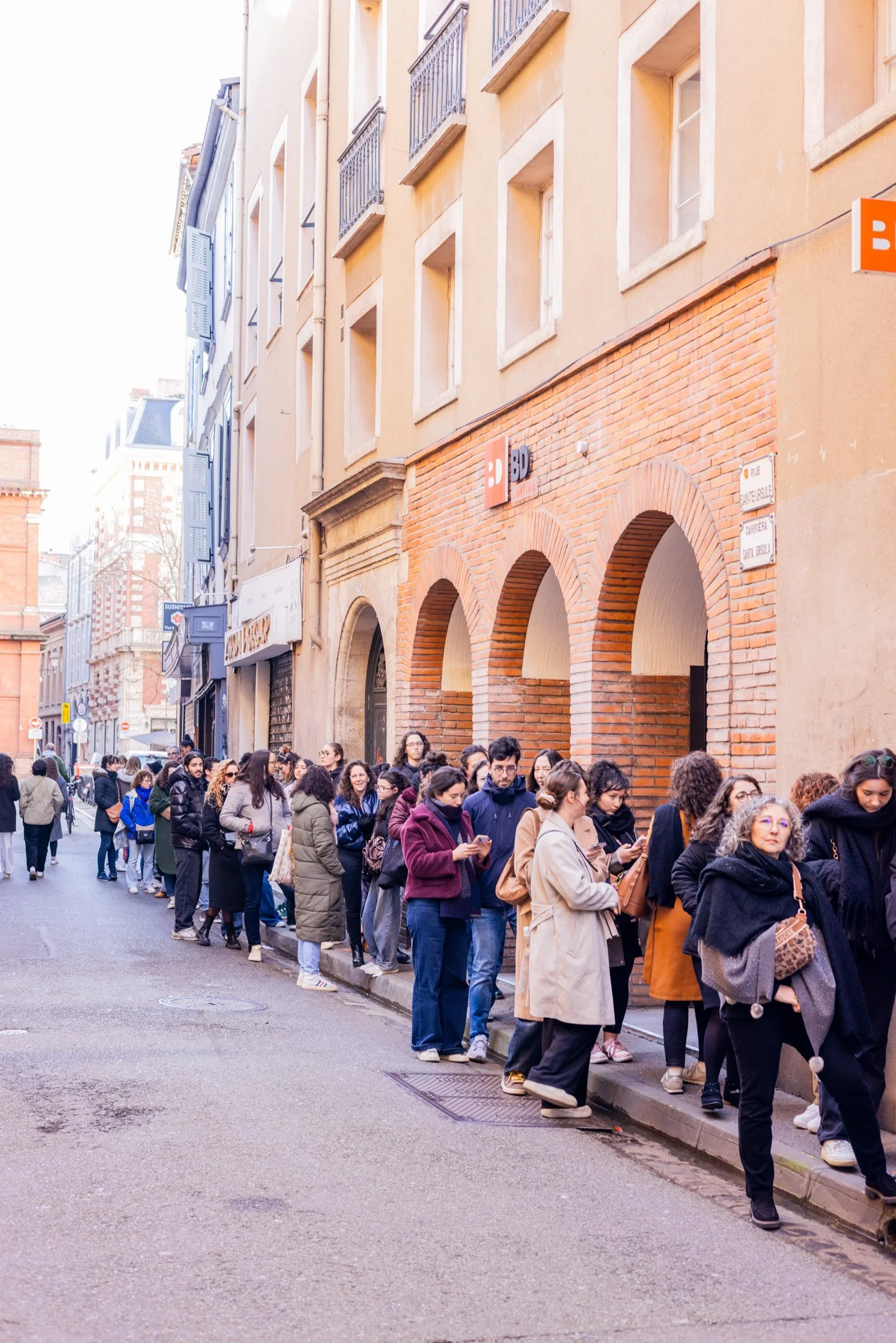 Une longue file d'attente de personnes devant un bâtiment avec des arches en briques à Paris, rue Saint-Florent, en France.