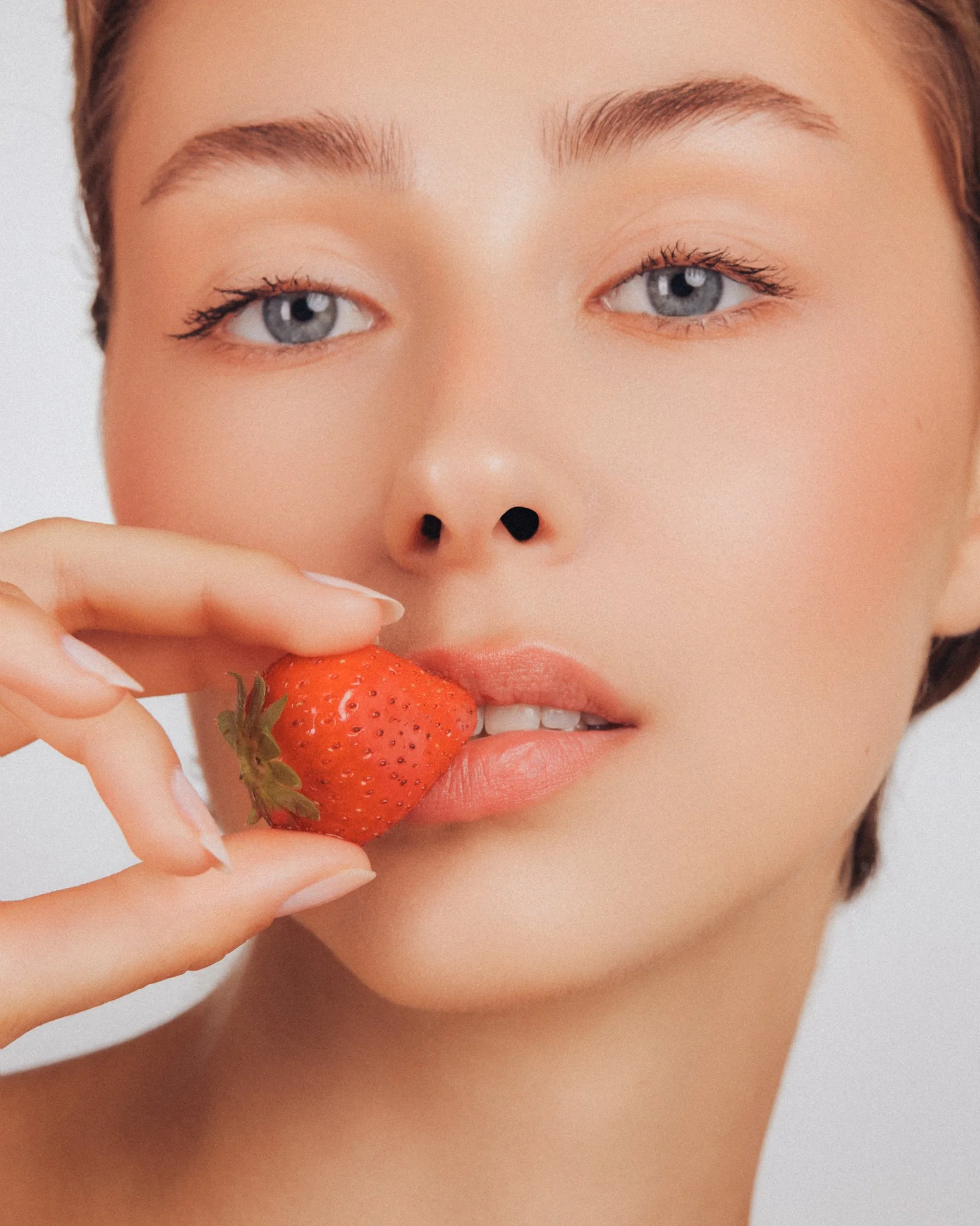 Une personne qui tient une fraise rouge près de sa bouche et son visage