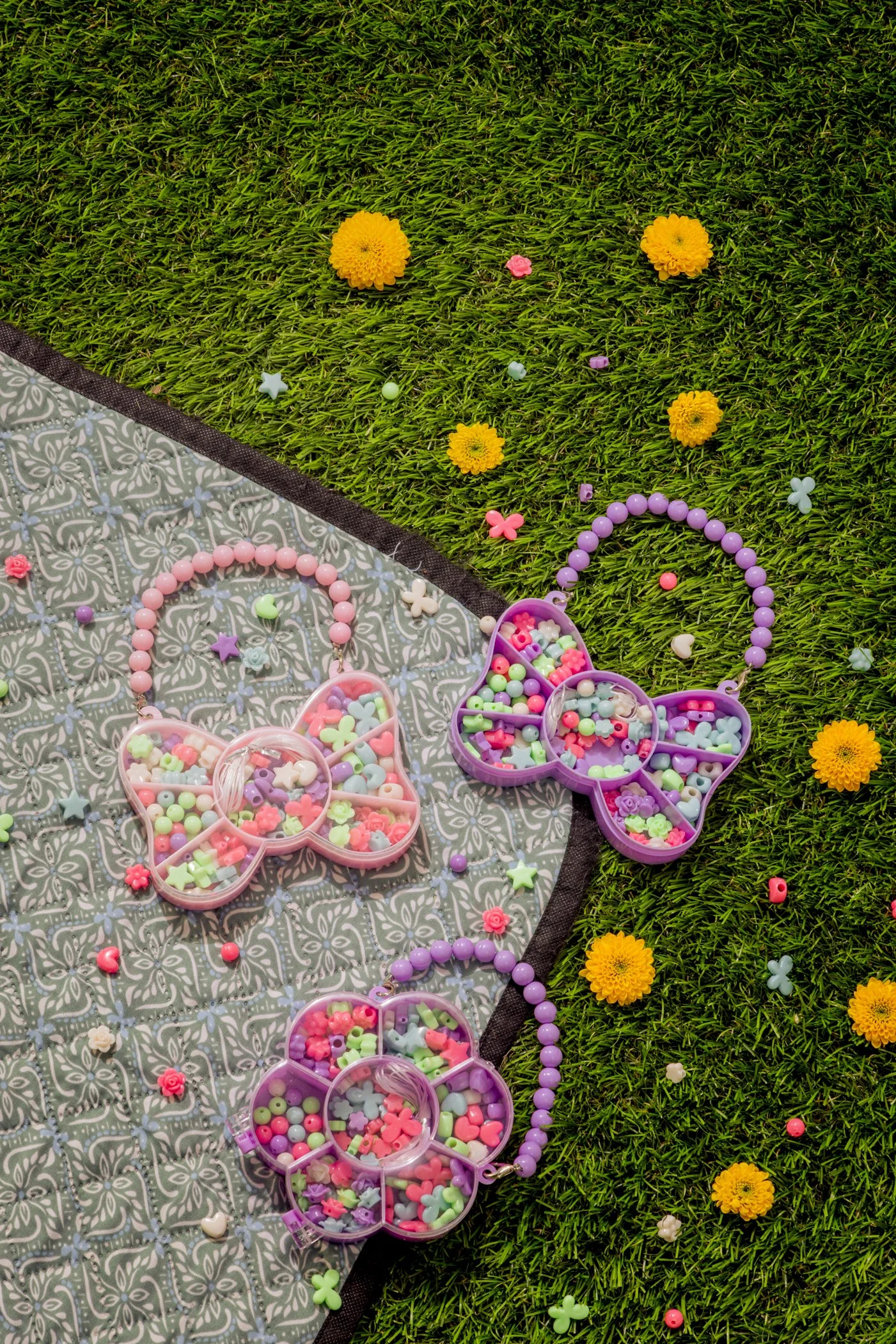 Garnitures colorées en plastique pour bijoux ou loisirs créatifs, disposées sur une surface en toile et sur de la pelouse avec des fleurs jaunes.