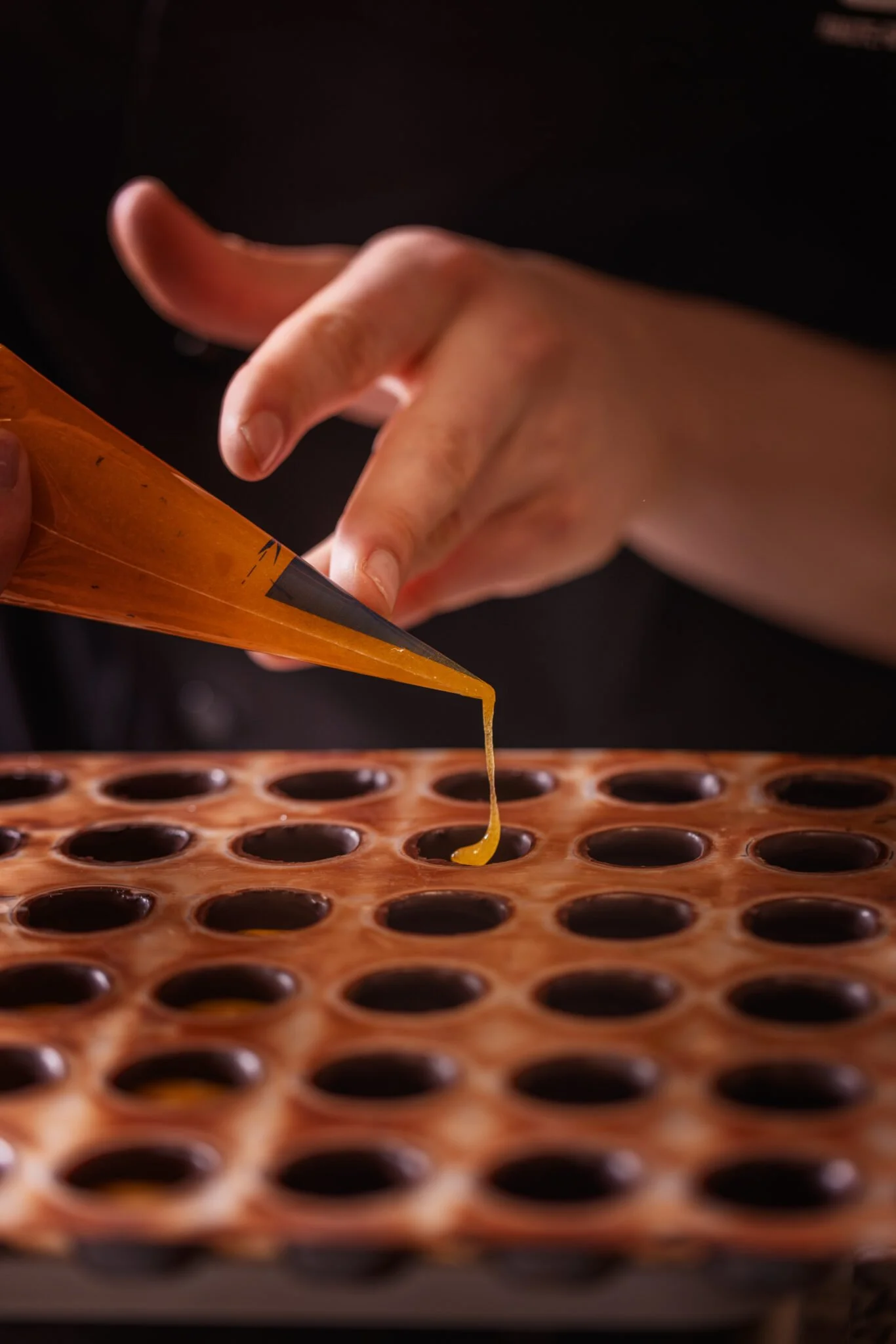 Une main verse du miel liquide dans un moule à bonbons en silicone orange perforé.
