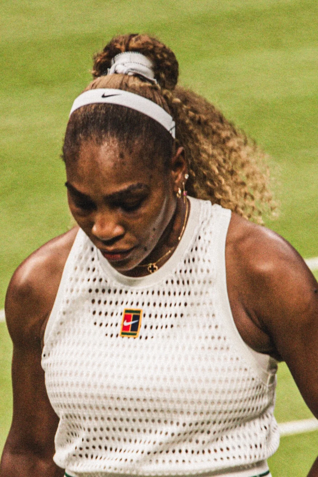 Une femme athlète portant un débardeur blanc en filet, avec un badge aux couleurs de la Belgique, lors d'une compétition sur un terrain de sport, semblant être fatiguée ou concentrée.
