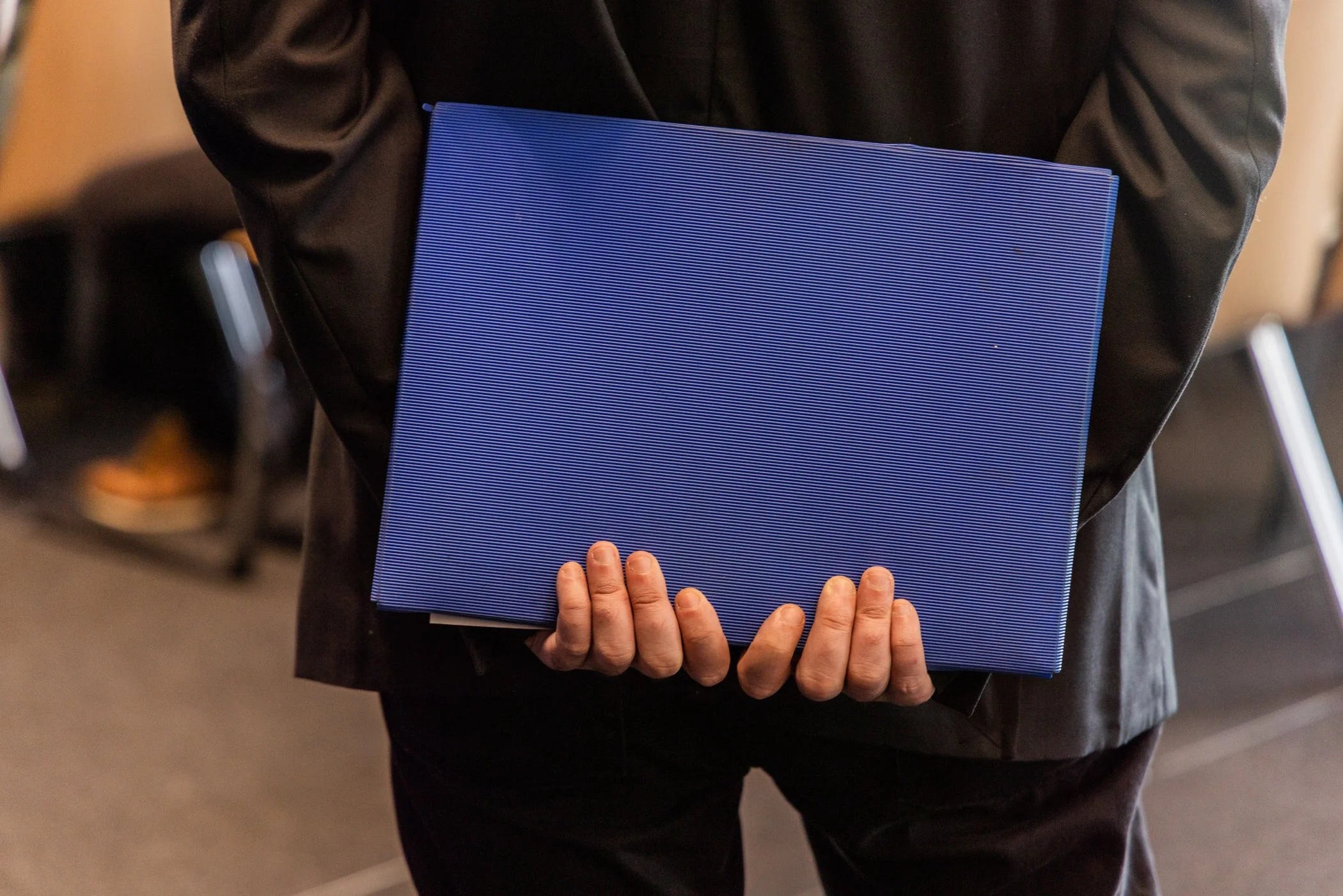 Personne tenant un classeur bleu dans une main et d'autres mains en dessous, dans un lieu intérieur.