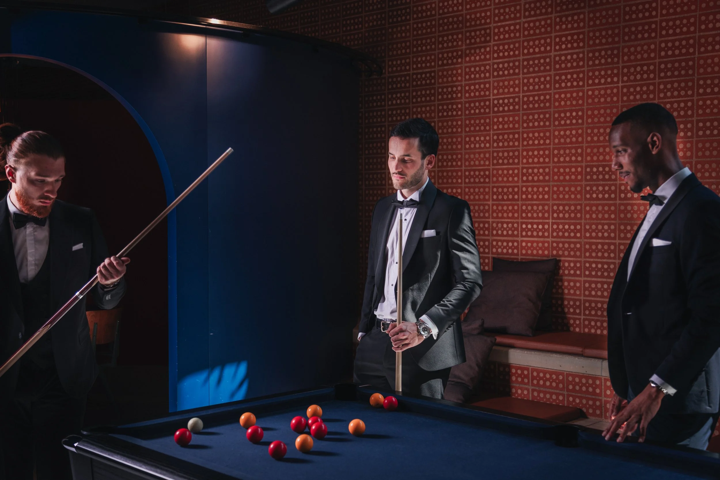 Trois hommes en smokings jouent au billard dans une pièce élégante.