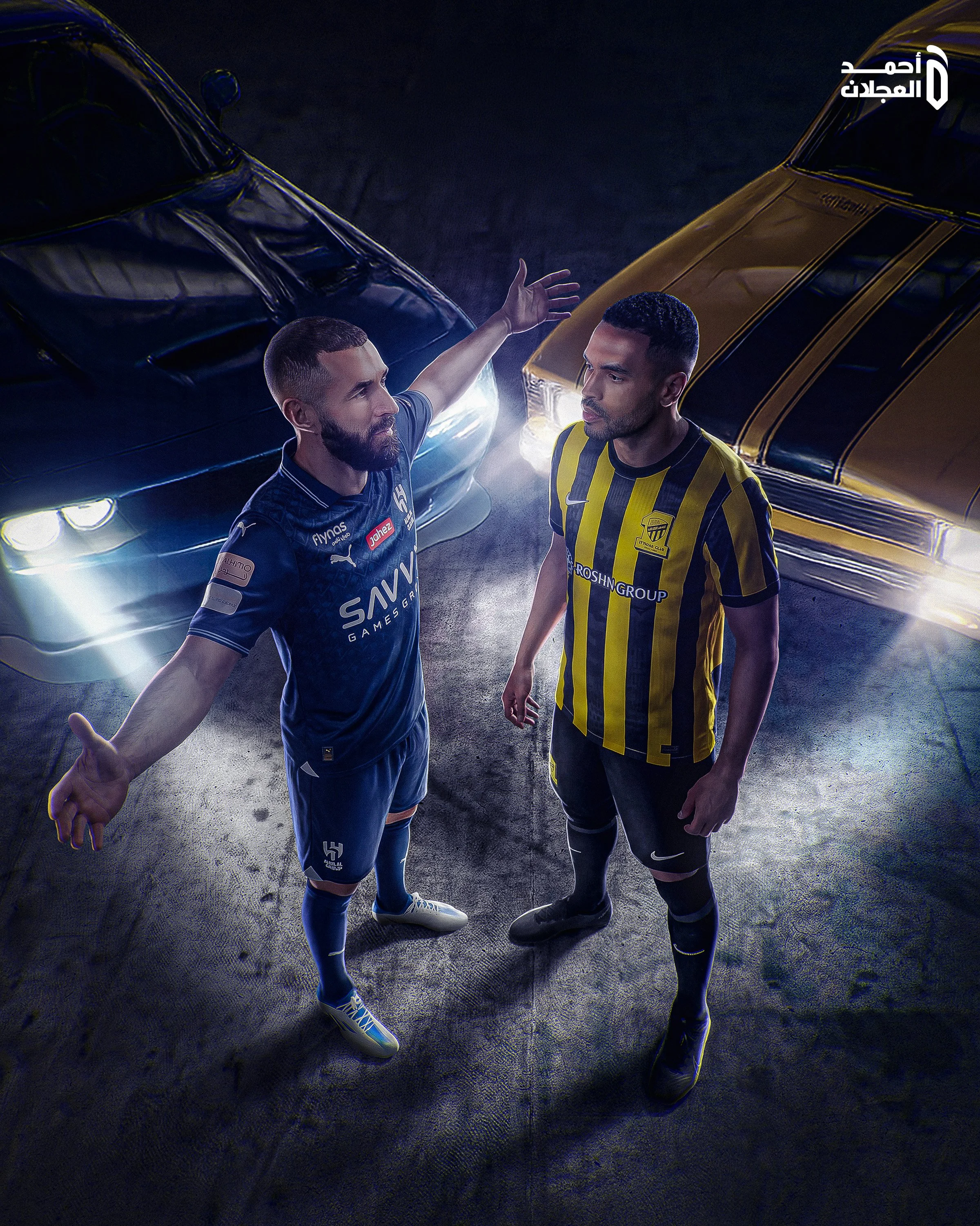 Two male soccer players in uniform standing face-to-face on a dark field, with one extending his arm toward the other, and two cars parked behind them.