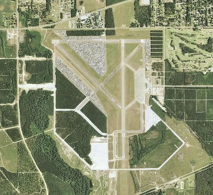 Aerial view of an airport with runways, taxiways, and surrounding green areas and fields.
