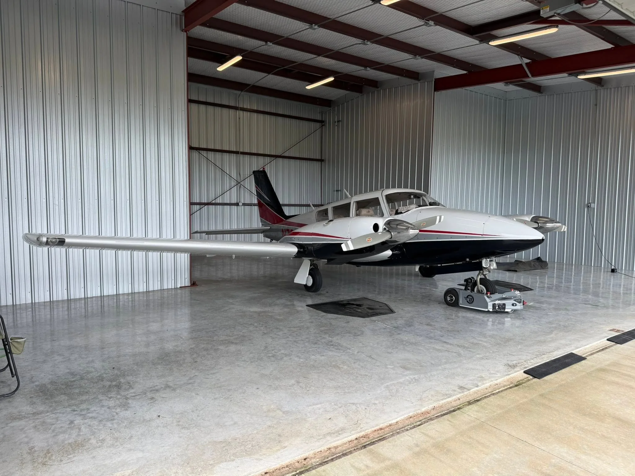 Aircraft inside a spacious hangar with a polished concrete floor, metal walls, and exposed ceiling beams. Equipment is placed near the airplane.
