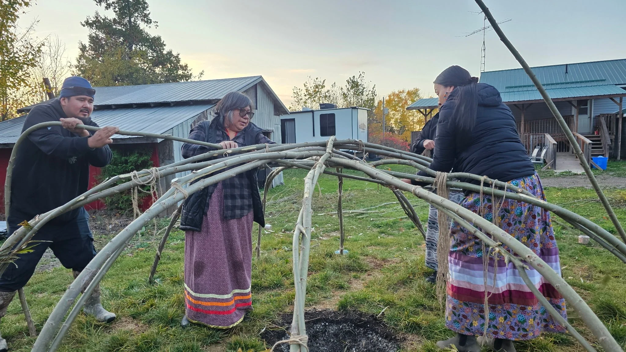 Four people working on constructing a wooden frame outdoors in a yard with houses and trees in the background.