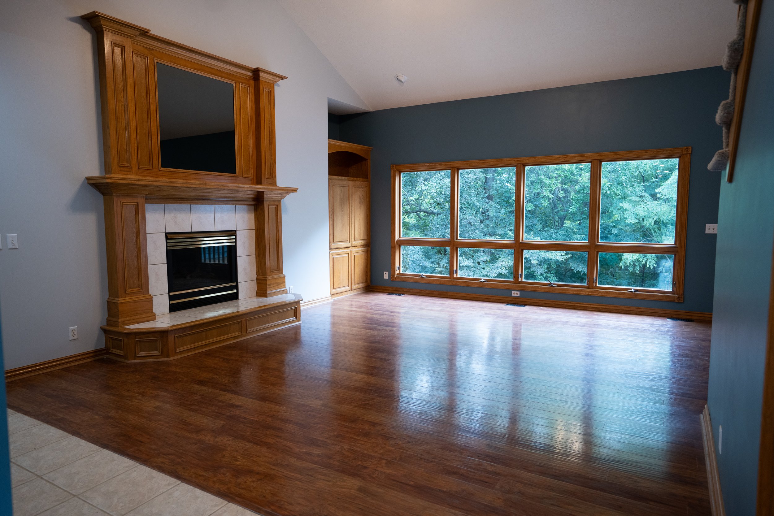 Open living room with wooden floors, large windows, and a fireplace on the left side.