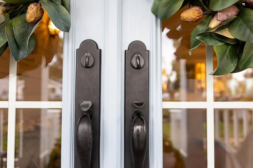 Close-up of double glass doors with black handles and greenery with brown seed pods above the doors.
