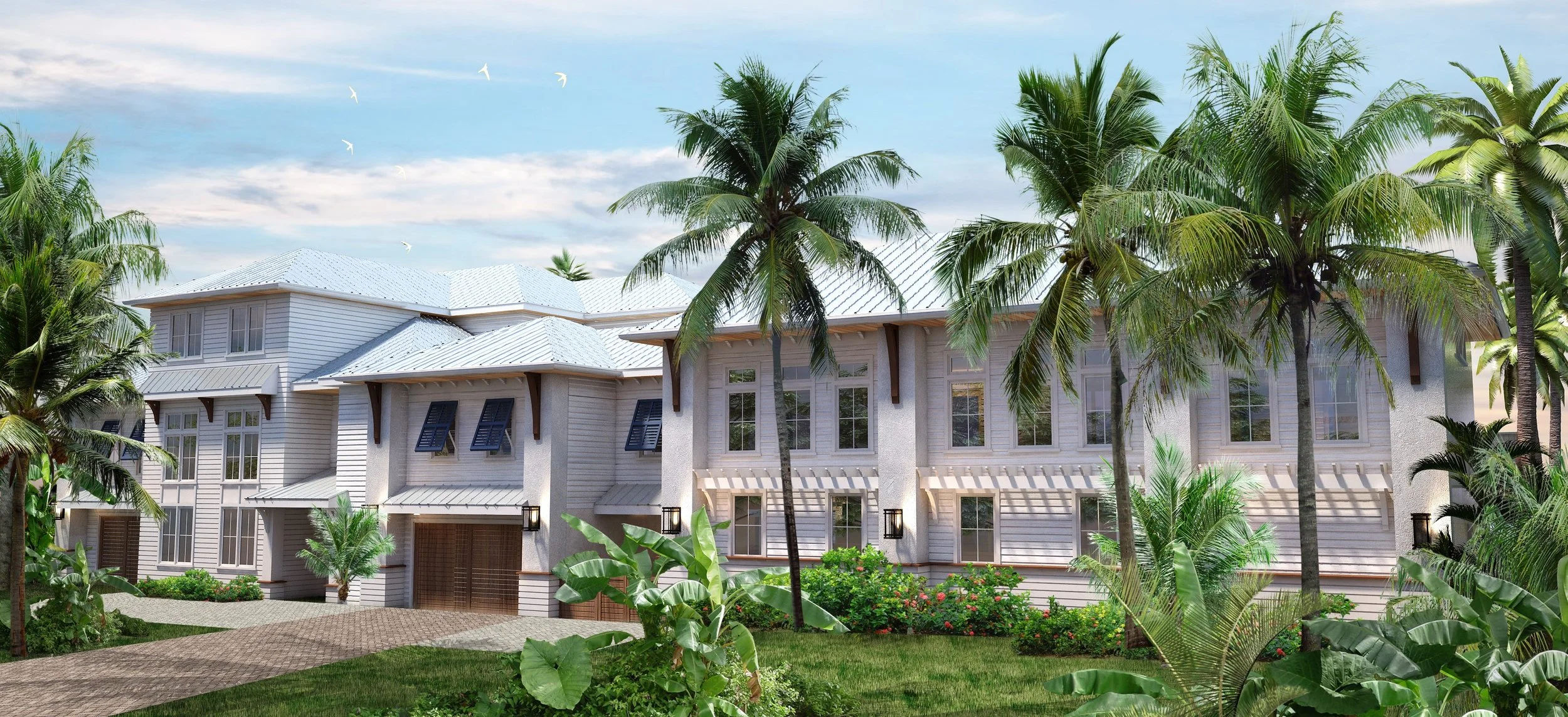 A large white house with multiple windows and a garage, surrounded by green palm trees and lush tropical plants, under a blue sky with some clouds.