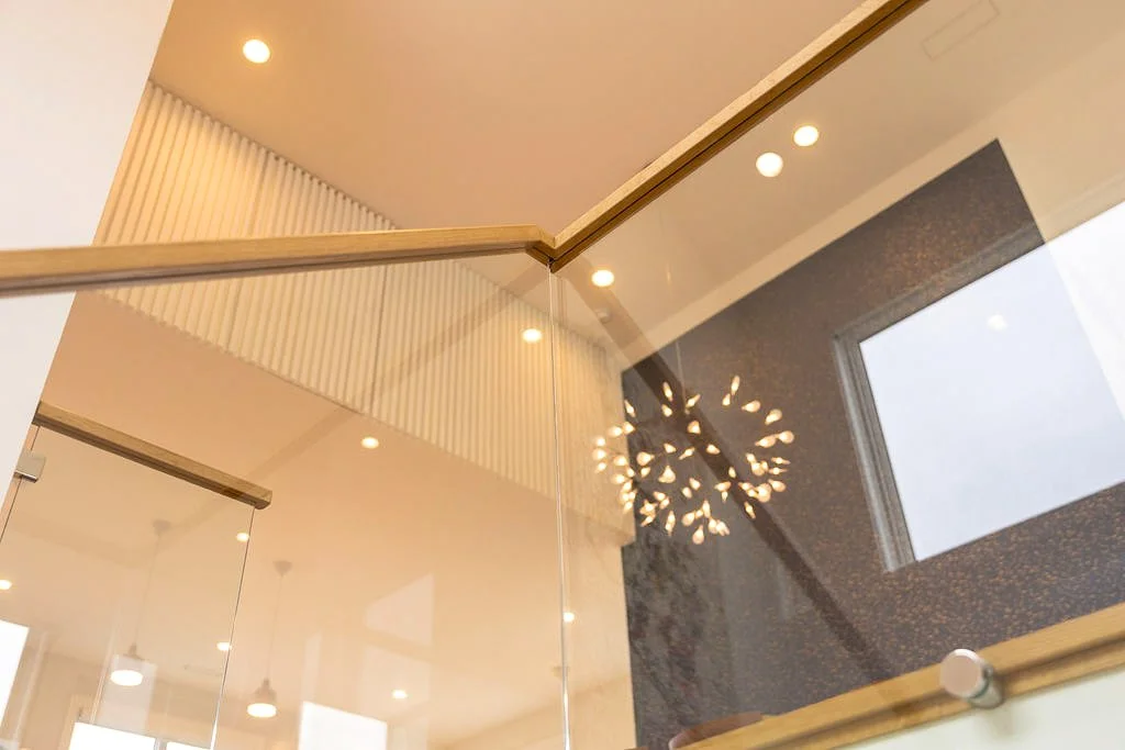 Interior view showing a ceiling with recessed lights, a modern chandelier, a textured dark wall, and a window with daylight.