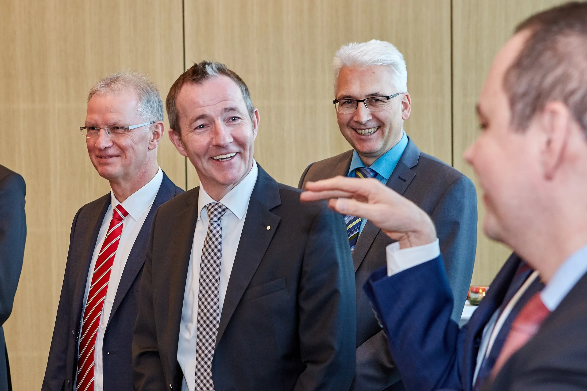Eine Gruppe von Männern in formeller Kleidung, die sich bei einem Treffen unterhalten, lachend und sich unterhaltend in einem Raum mit Holzwänden.