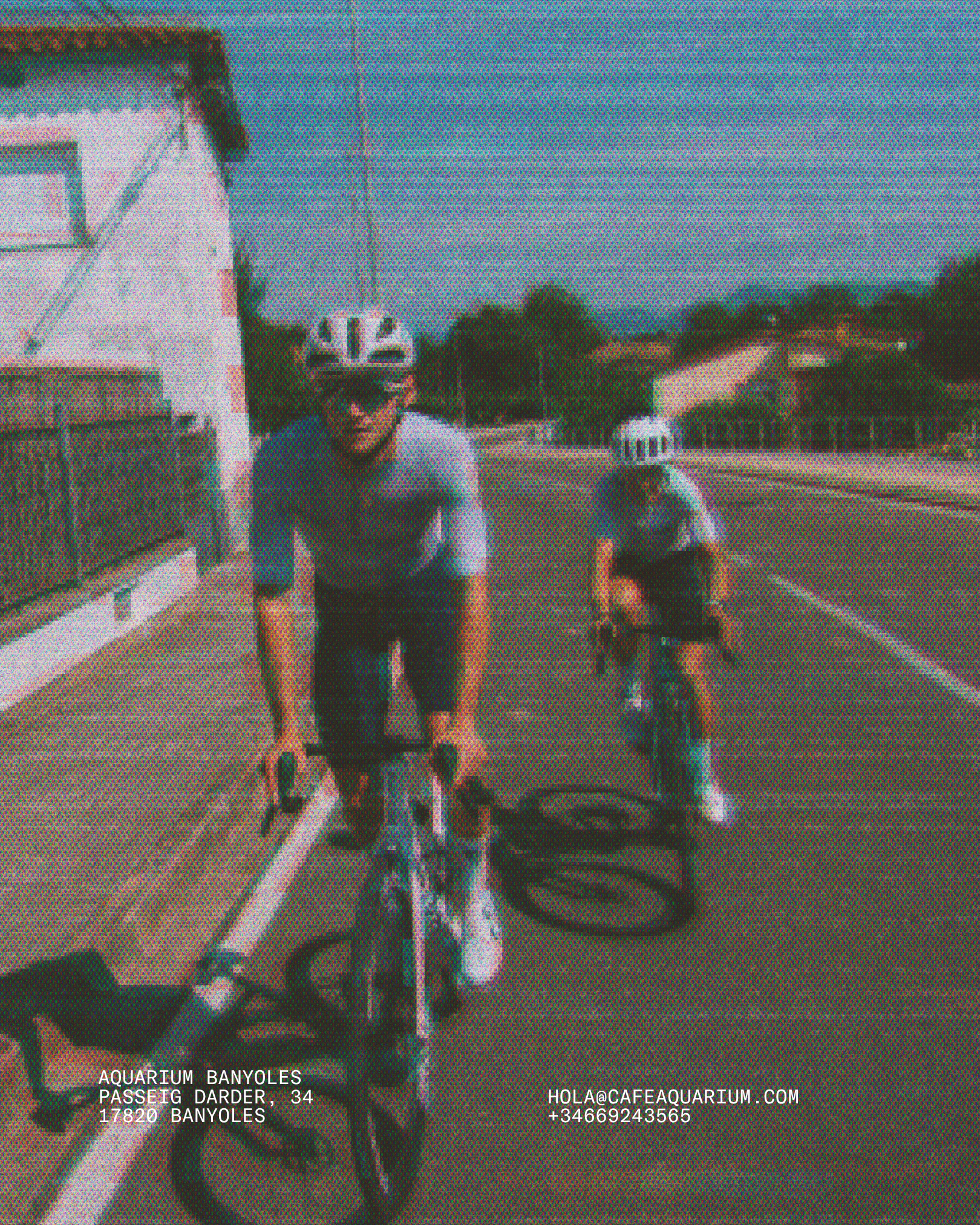 People riding bicycles at a bike path near the beach with a railing in the foreground and buildings, trees, and a cloudy sky in the background. Text overlay includes contact and location information for Aquarium Banyoles.
