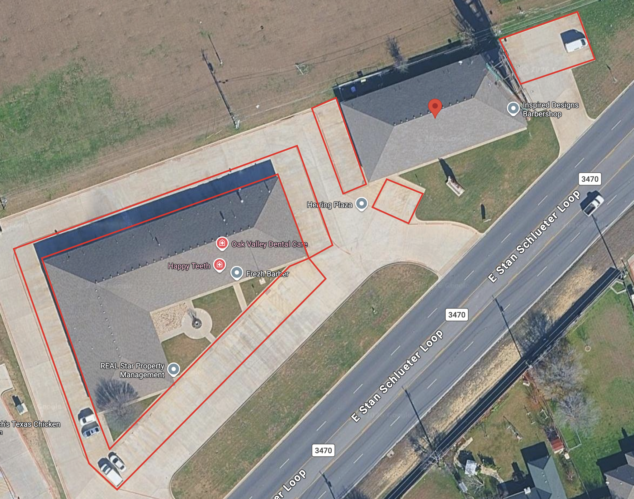 Aerial view of a commercial building with a parking lot and an adjacent grassy area. Several cars are parked, and red outlines mark specific areas around the building. Nearby streets are labeled, and the building houses businesses including a barbershop and dental care.