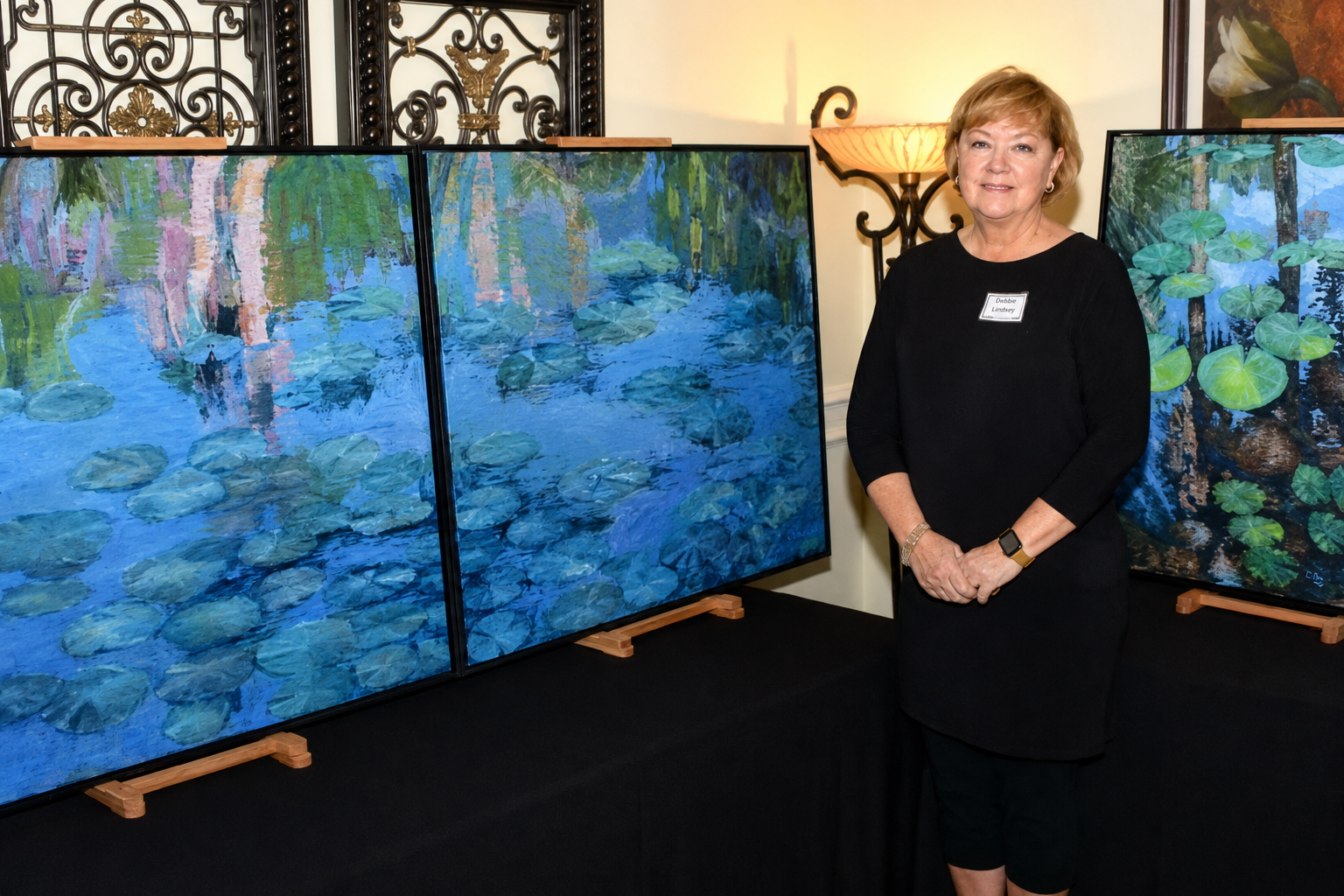 Debbie Lindsey standing beside her lily pond paintings at an art exhibition