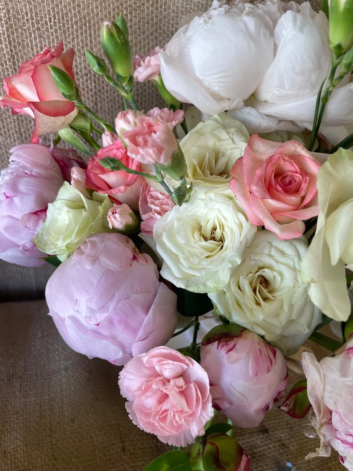 A bouquet of pink and white flowers, including roses, gardenias, and carnations, arranged against a textured beige background.