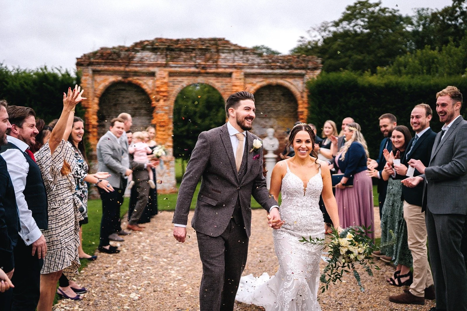 A bride and groom walking hand in hand during their wedding celebration, surrounded by friends and family outdoors.