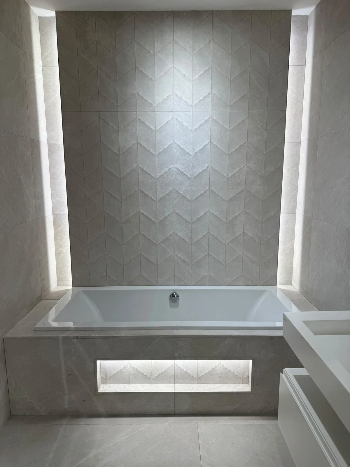 Bathroom with a built-in bathtub and beige tiled walls, featuring a central decorative wall with geometric tile pattern.