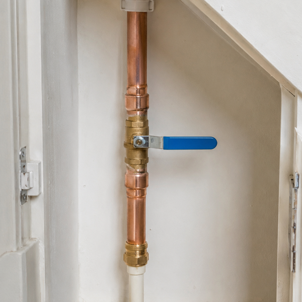 Close-up of a copper water pipe with a brass valve and a blue handle inside a white cabinet.