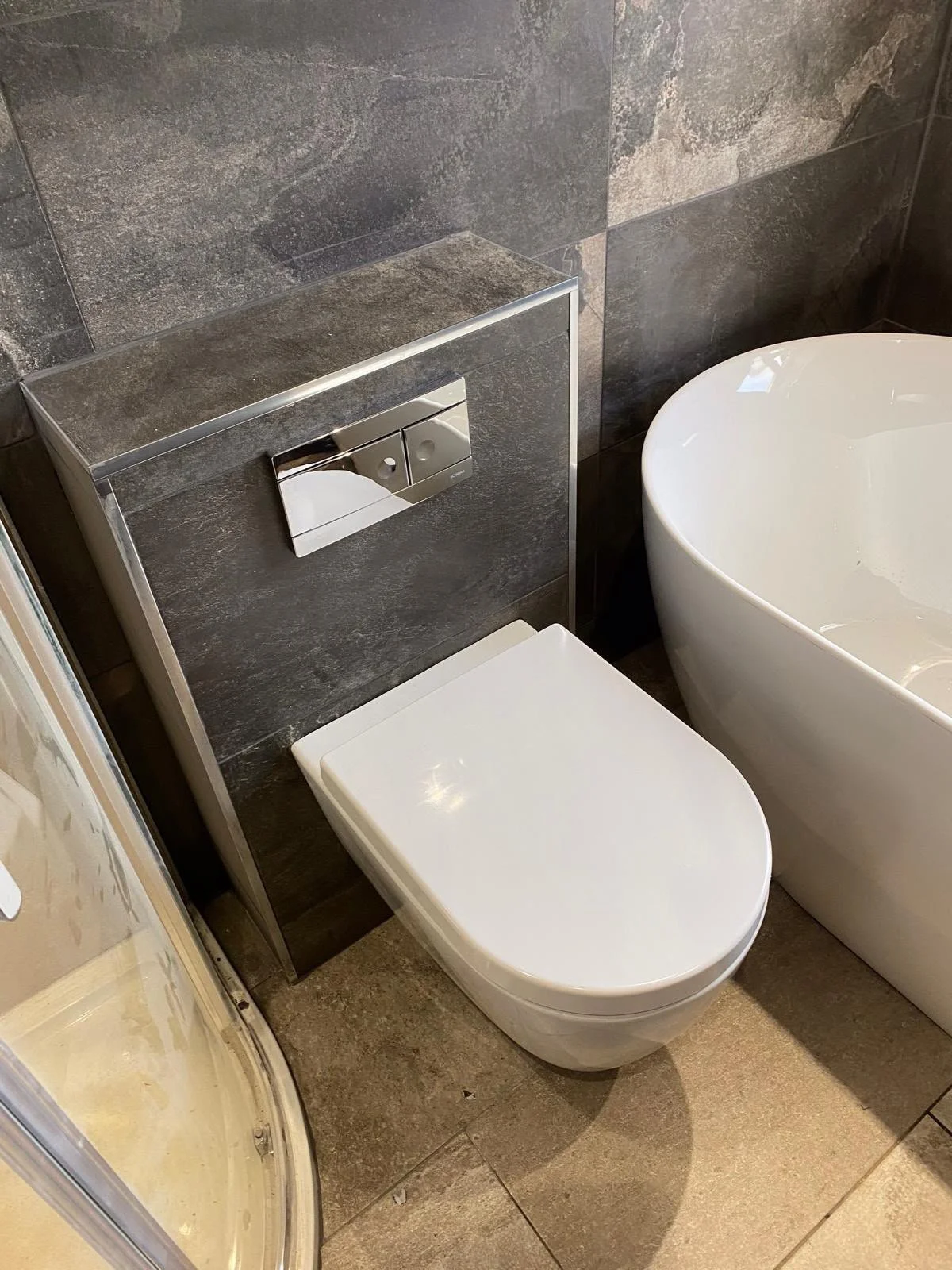 Close-up of a modern bathroom with a wall-mounted toilet, a toilet paper holder, and a bathtub with dark tile walls.