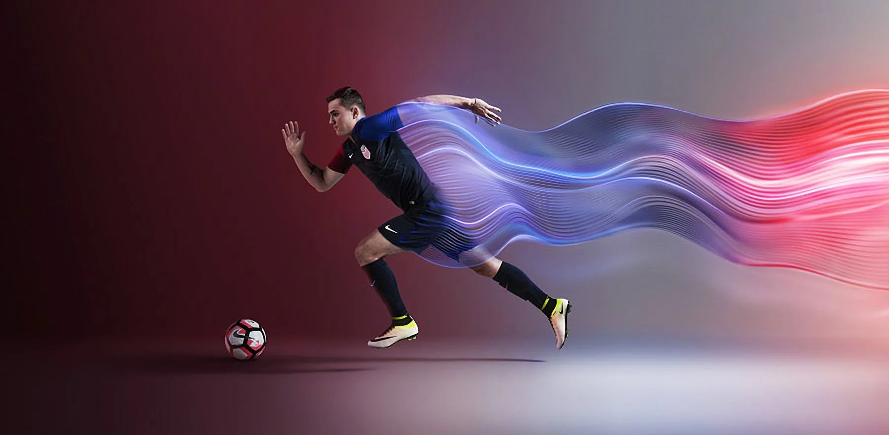A soccer player in a black and blue uniform running toward a soccer ball with a digital streak trail behind him.