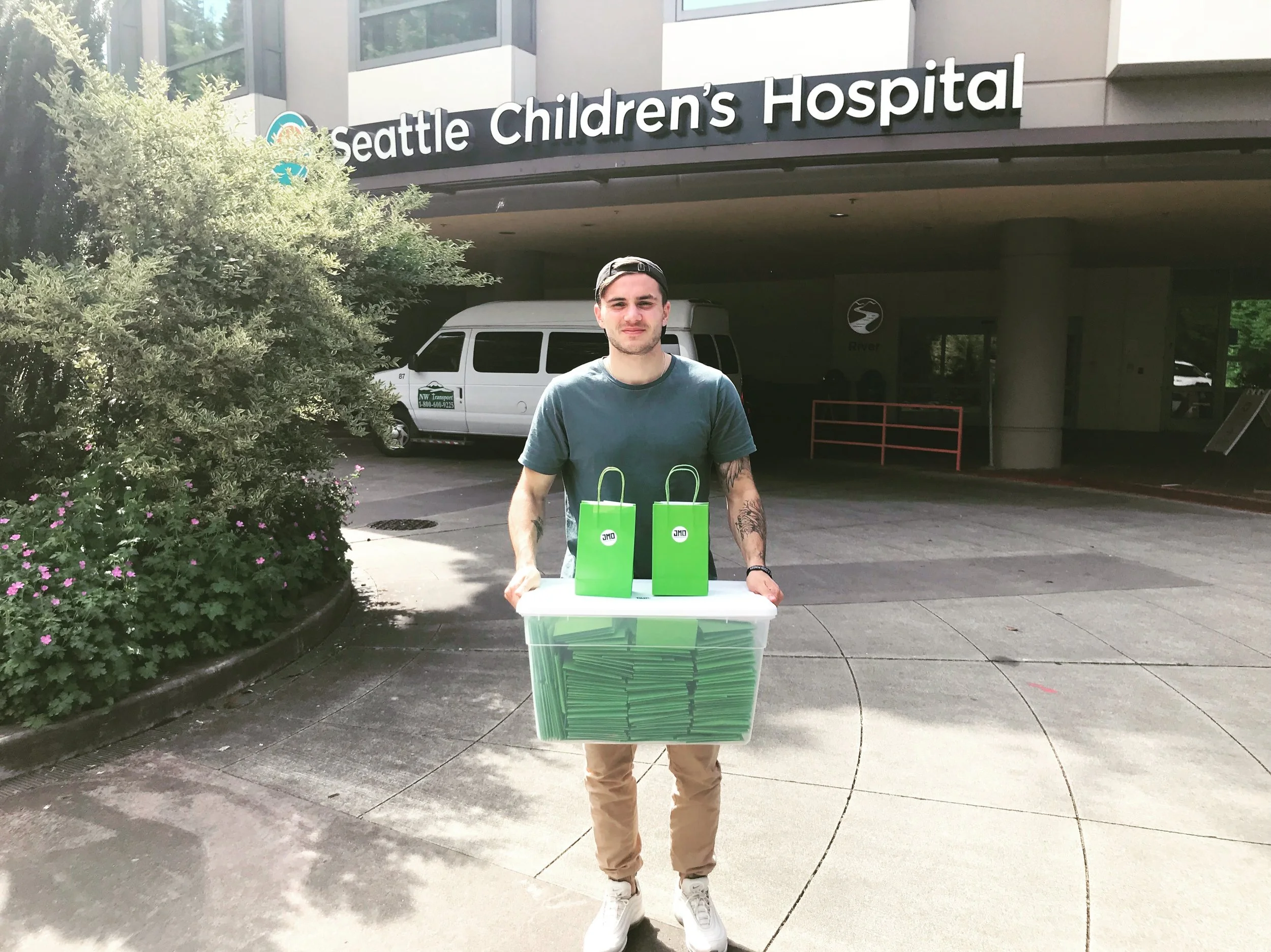 A young man holding a large container filled with green folders outside Seattle Children's Hospital.
