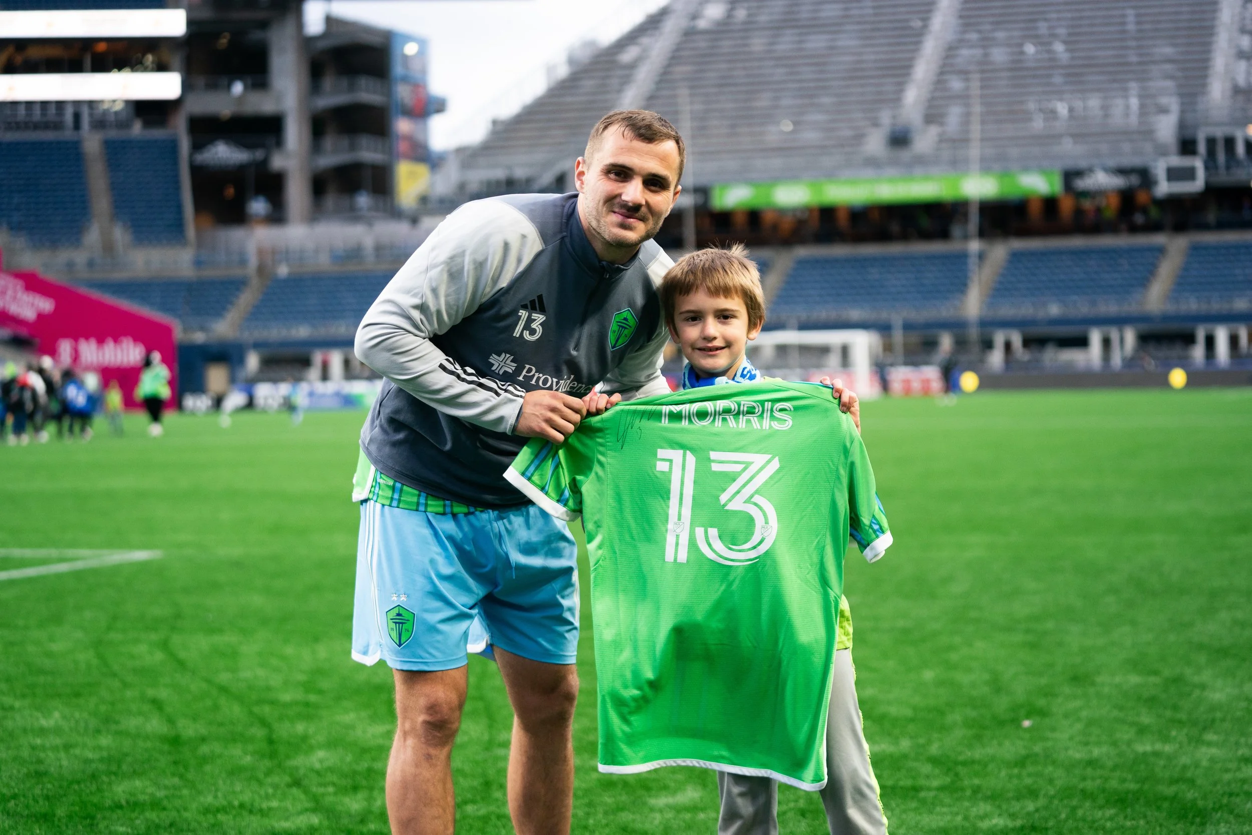A man and a young boy on a soccer field holding a green soccer jersey with the name 