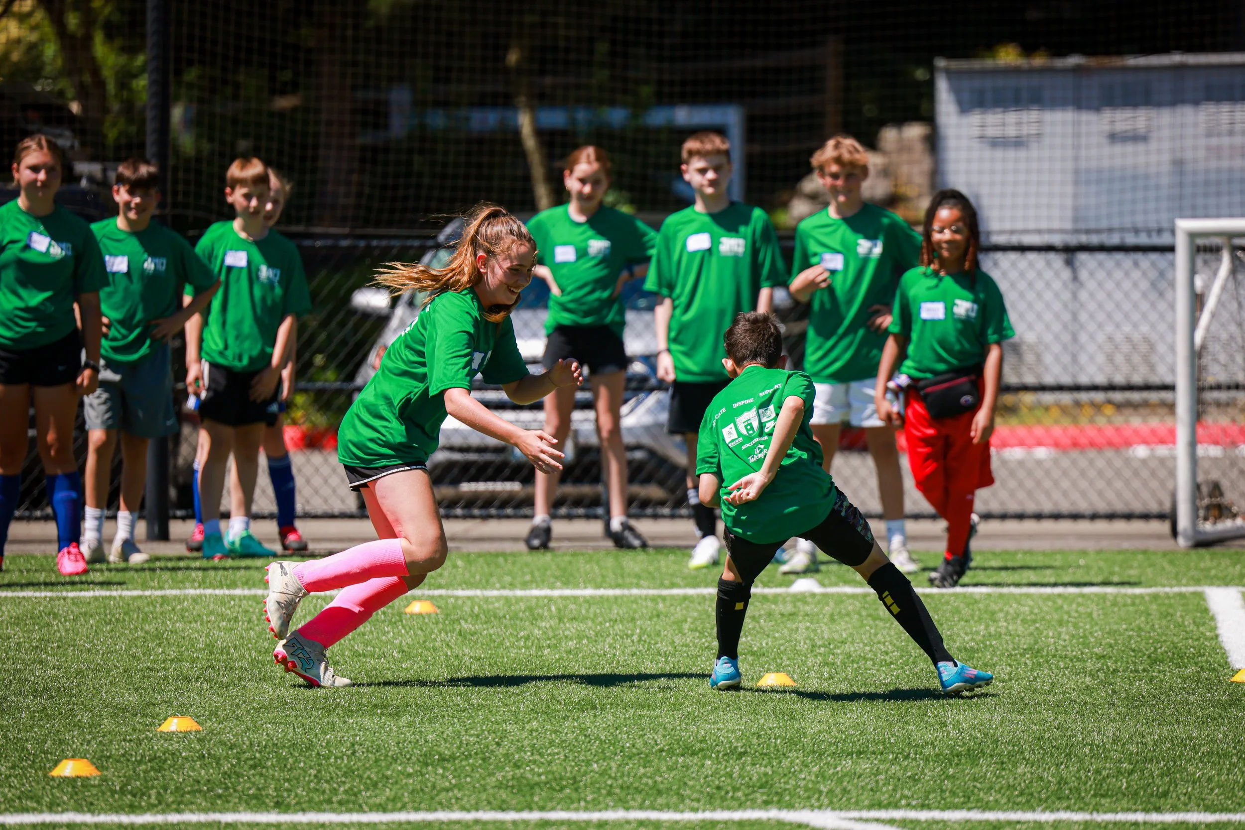 Children participating in a sports activity on a field, with some running and others standing nearby, all wearing green shirts.