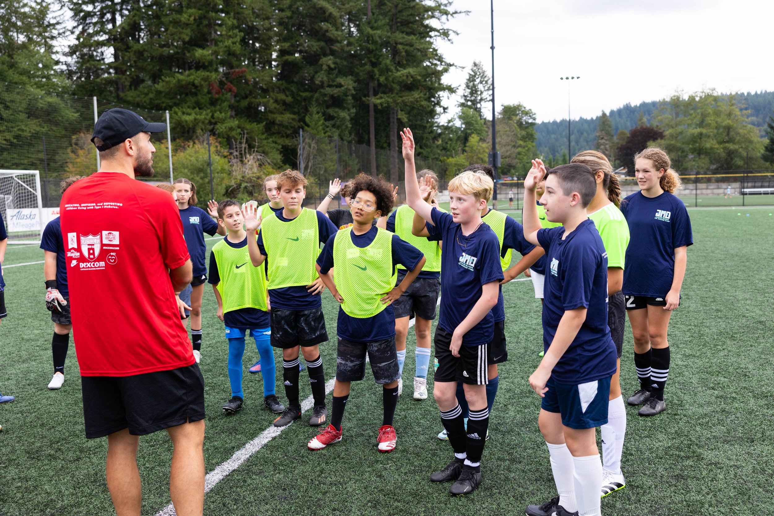 Young female soccer players receiving instructions from their coach on a soccer field with trees in the background.
