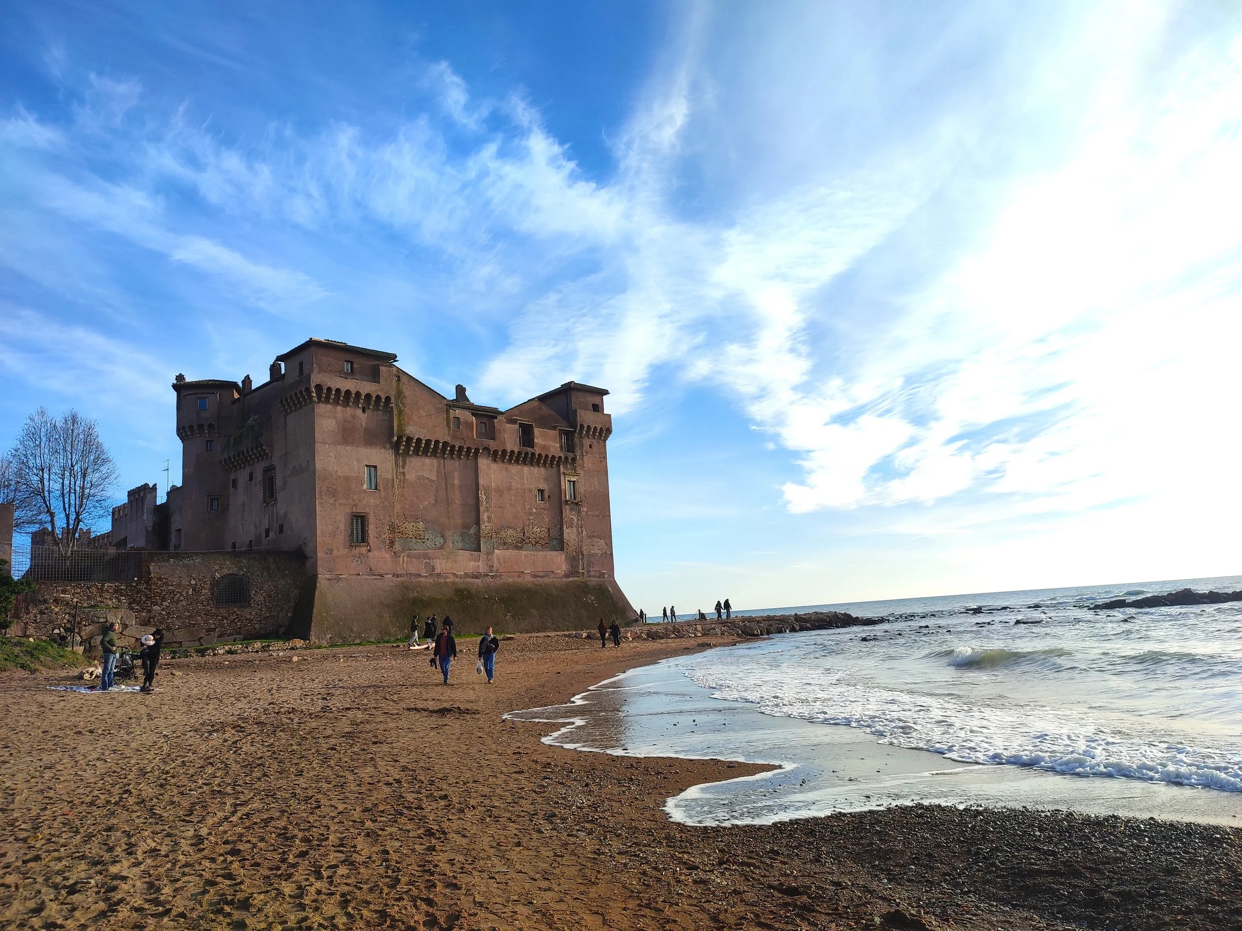 Castello su una spiaggia con persone che camminano vicino alla riva, mare e cielo con nuvole sparse