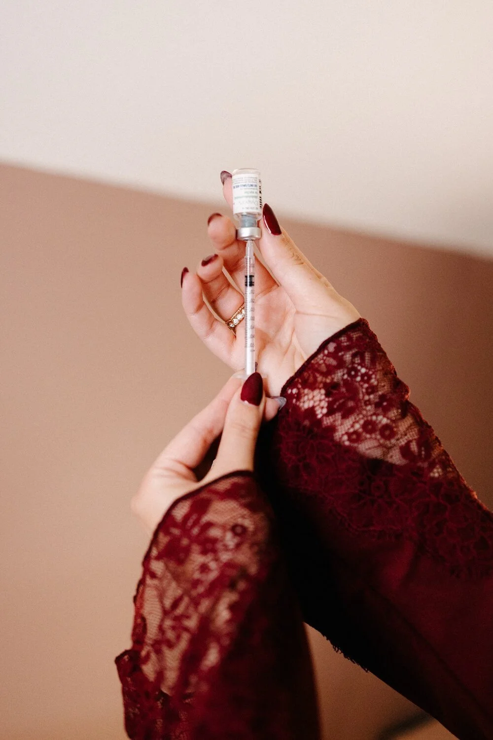 A person in a lace sleeve holding a syringe with a vaccine vial, preparing for a shot.