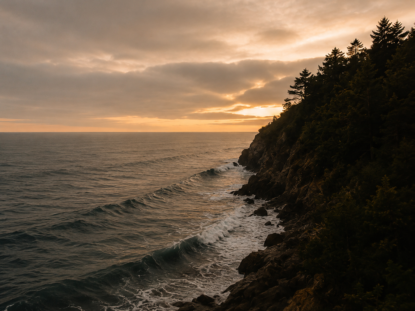 A scenic view of the ocean with gentle waves and a rocky, tree-covered cliff at sunset.