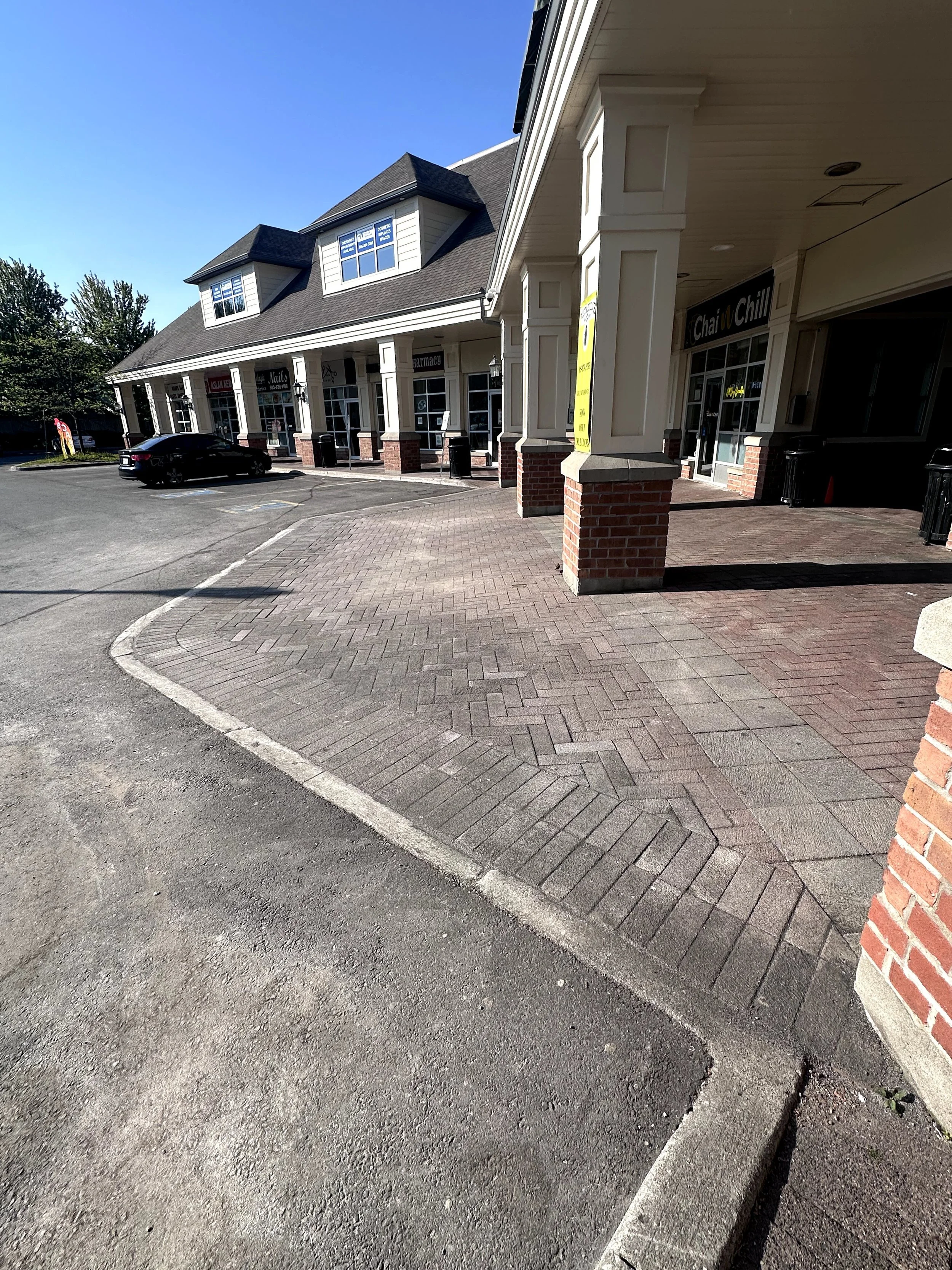 A strip mall with a parking lot and storefronts including a pharmacy and a nail salon.