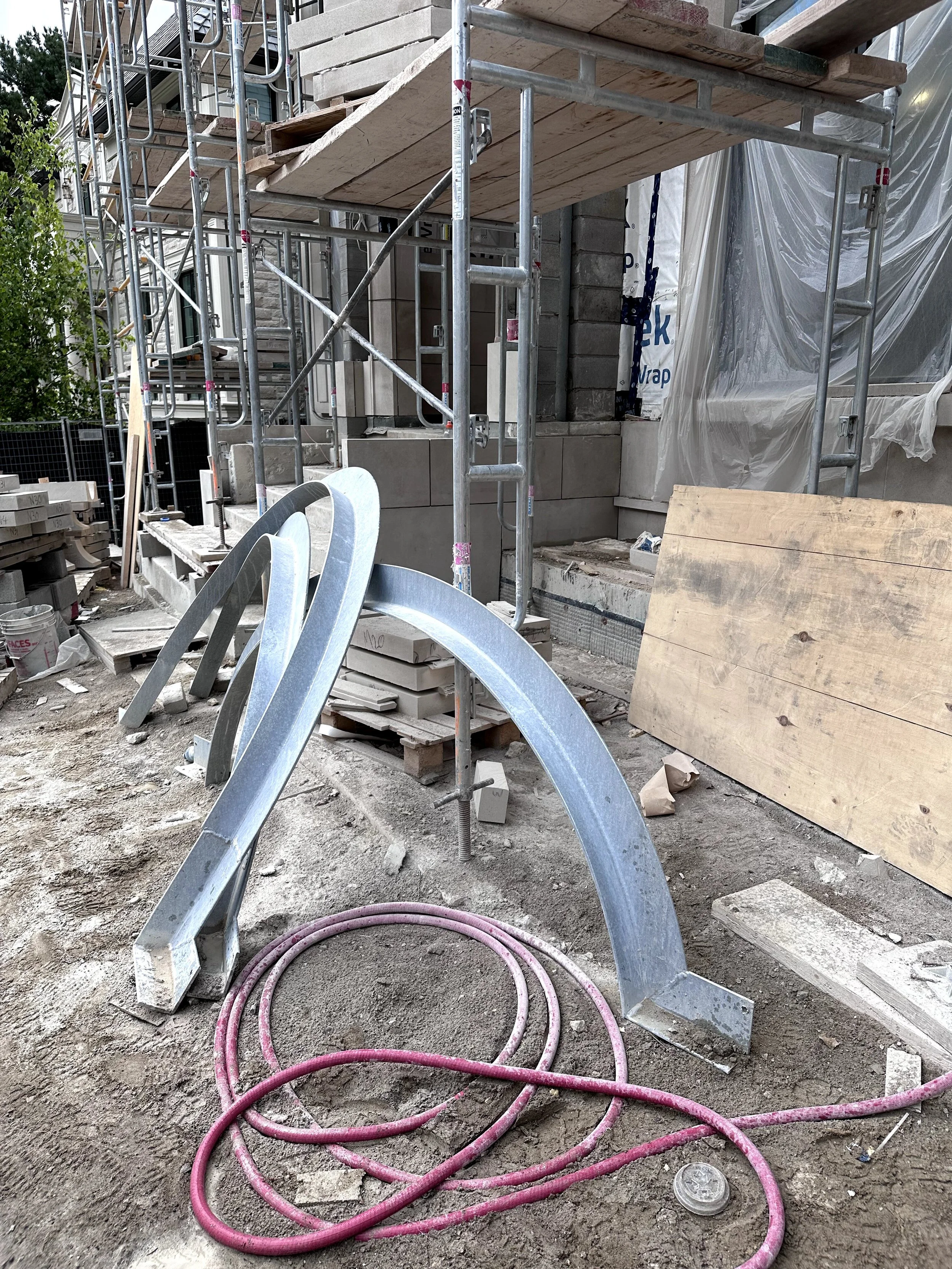 Construction site with scaffolding, wooden planks, construction materials, and pink cables on the ground.