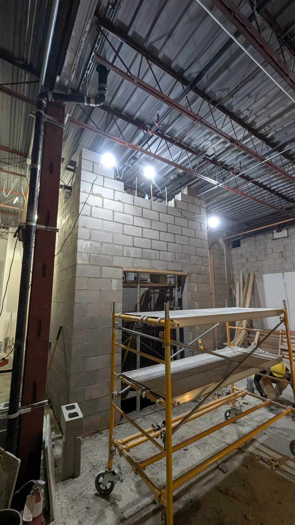 Construction site with scaffolding, cinder block walls, and steel beams in the ceiling, illuminated by bright lights.
