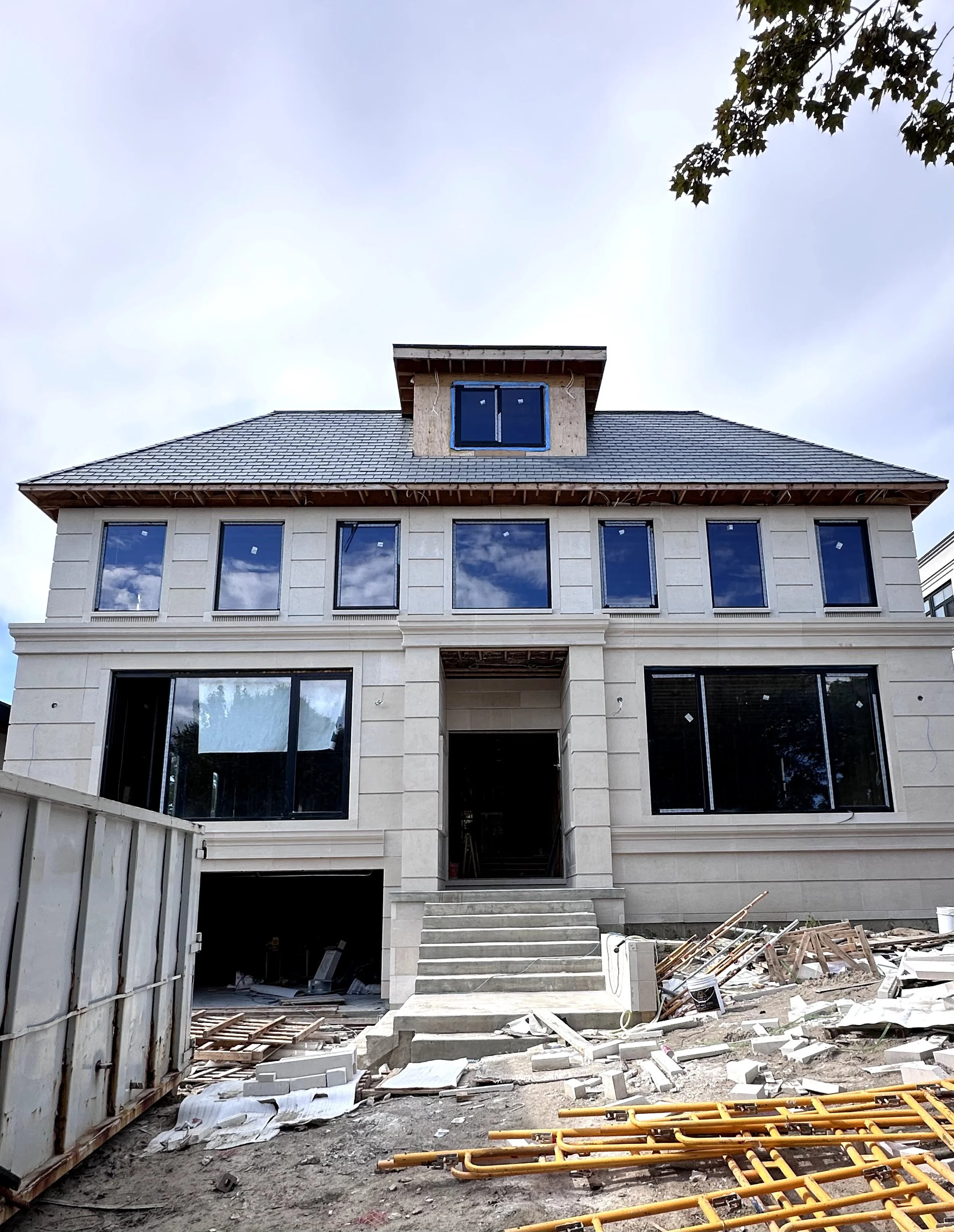 Under construction multi-story building with large windows, scaffolding, construction materials, and debris in the foreground.