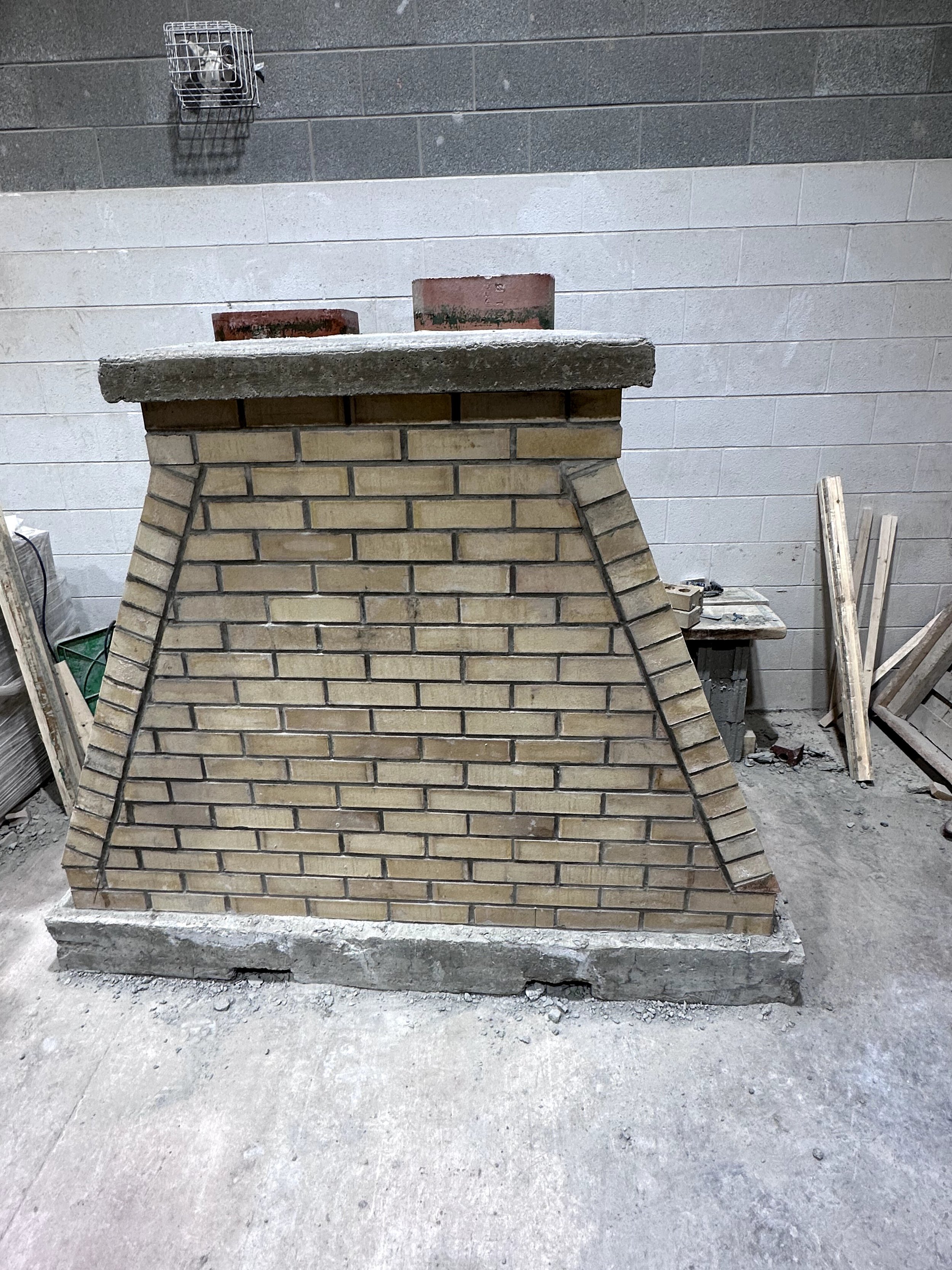 A brick fireplace under construction in an indoor setting, with construction materials and tools around it.