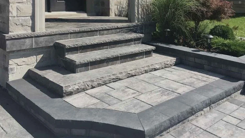 Stone steps and landing at the entrance of a house, with stone pavers on the ground and landscaping on the side.