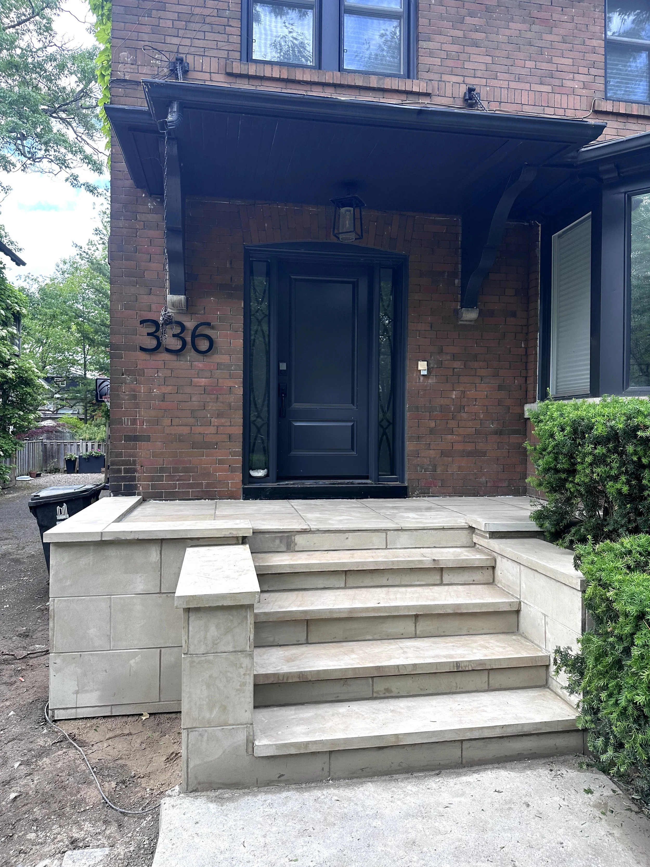 Front porch with stairs leading up to a black door, brick exterior, house number 336, and greenery on the side.