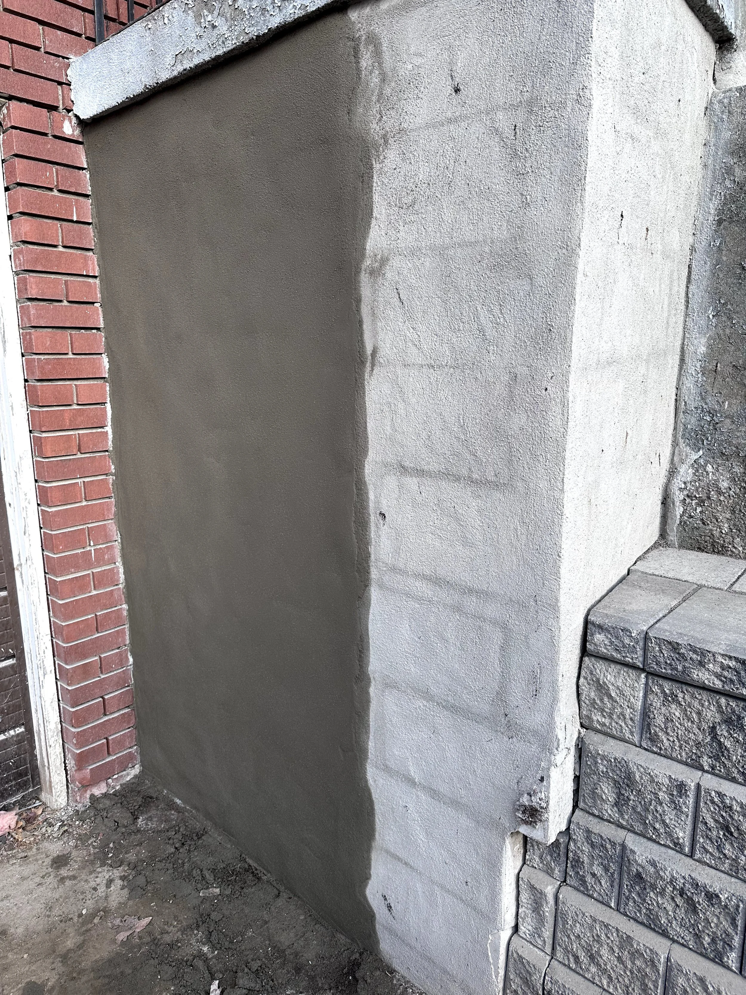 Building a wall with freshly poured gray cement on the lower part, bordered on the left by red bricks and on the right by stacked gray bricks.