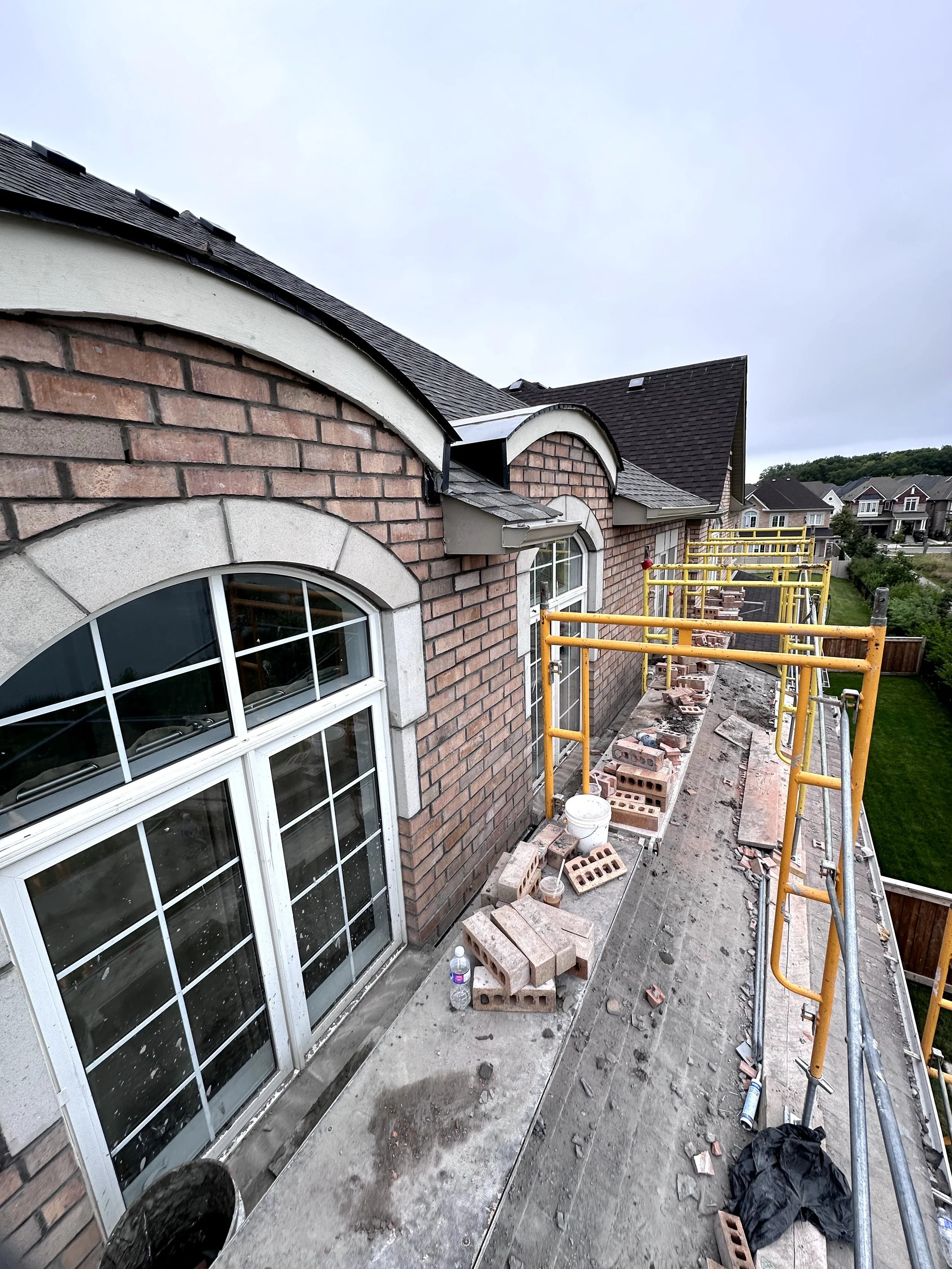 Construction site outside a brick house with scaffolding, bricks, and construction materials on the ground.