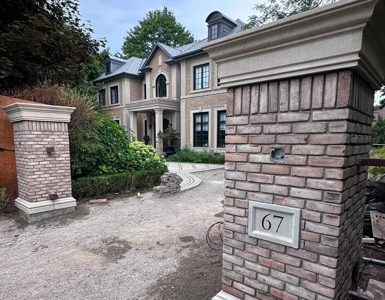 View of a large, elegant brick house behind a brick gate with the house number 67.