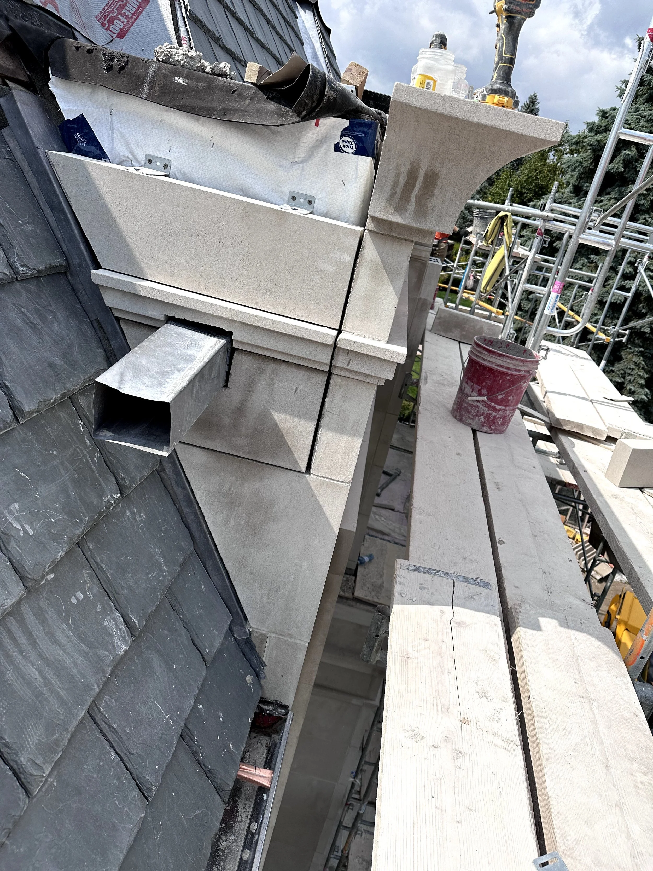 Construction site with stone fireplace, scaffolding, and work tools on a roof extension.