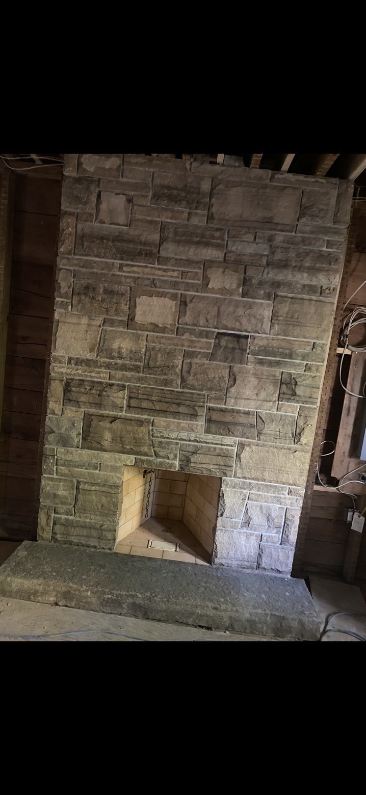 Stone fireplace with a hearth, in a room under construction or renovation, with visible electrical wiring on the side walls.
