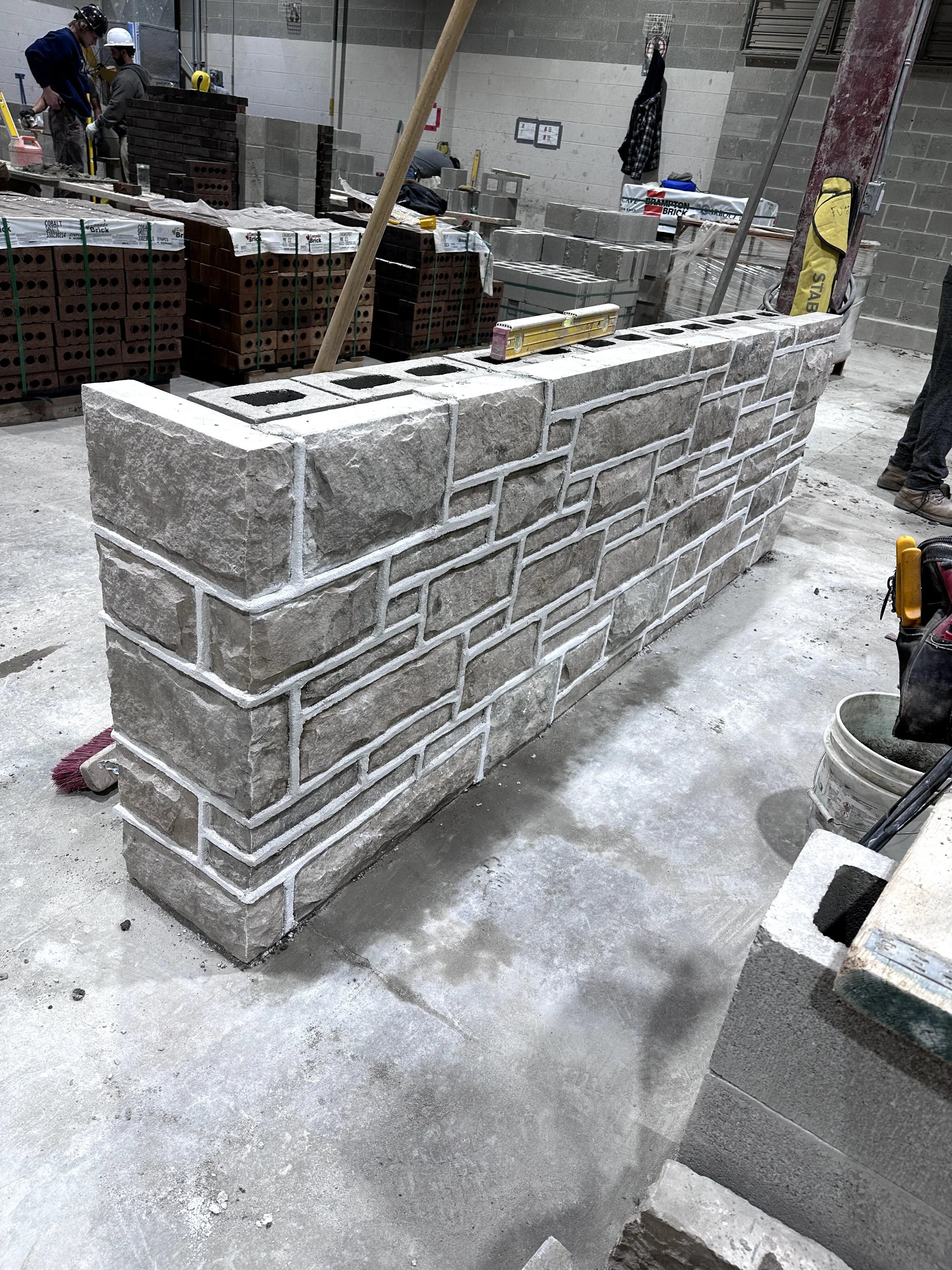 Construction site with workers building a brick wall and stacks of bricks in the background.