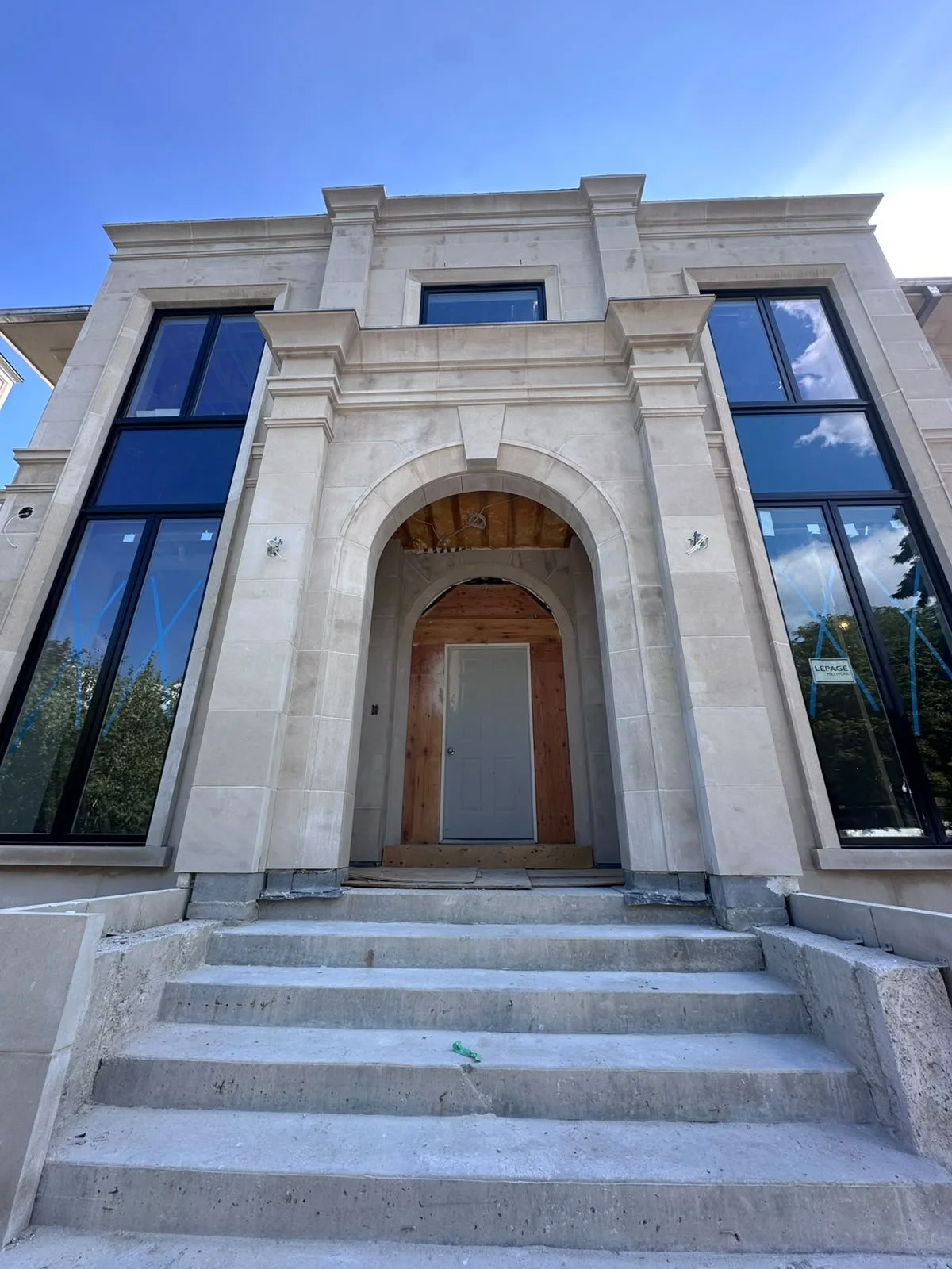 Modern house with large glass windows, a stone facade, and a small staircase leading to a front door with a wooden archway.