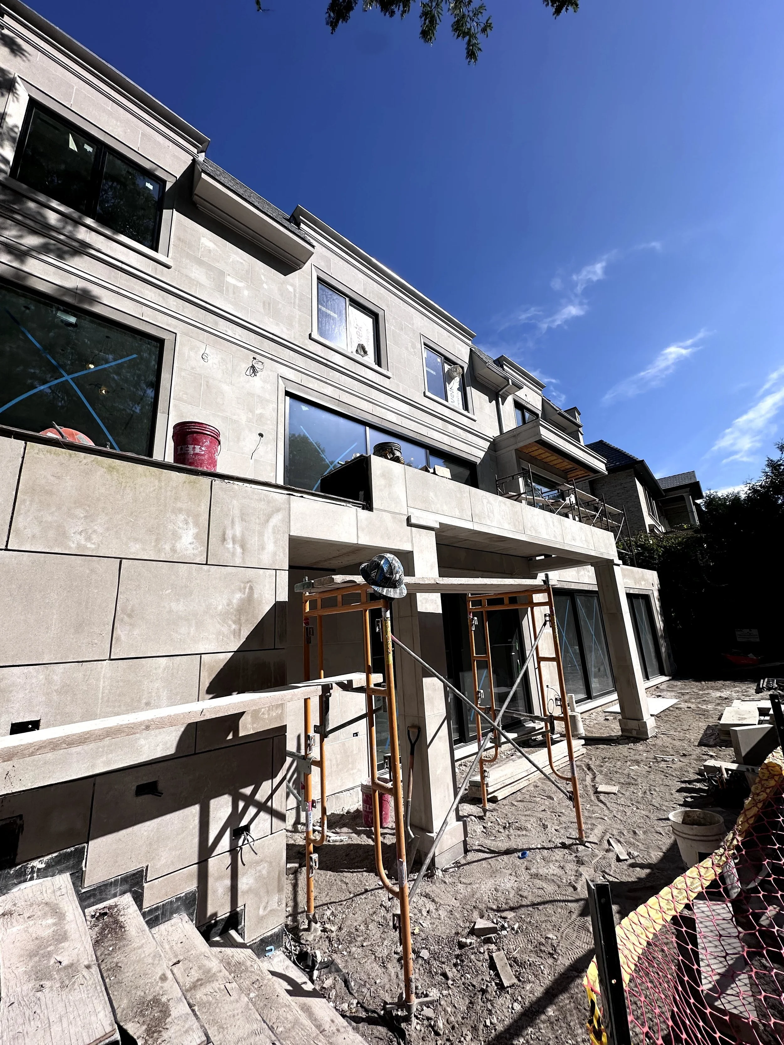 Under construction of a multi-story residential building, with scaffolding, construction tools, and debris visible on the ground, and the building's gray exterior walls and large windows.