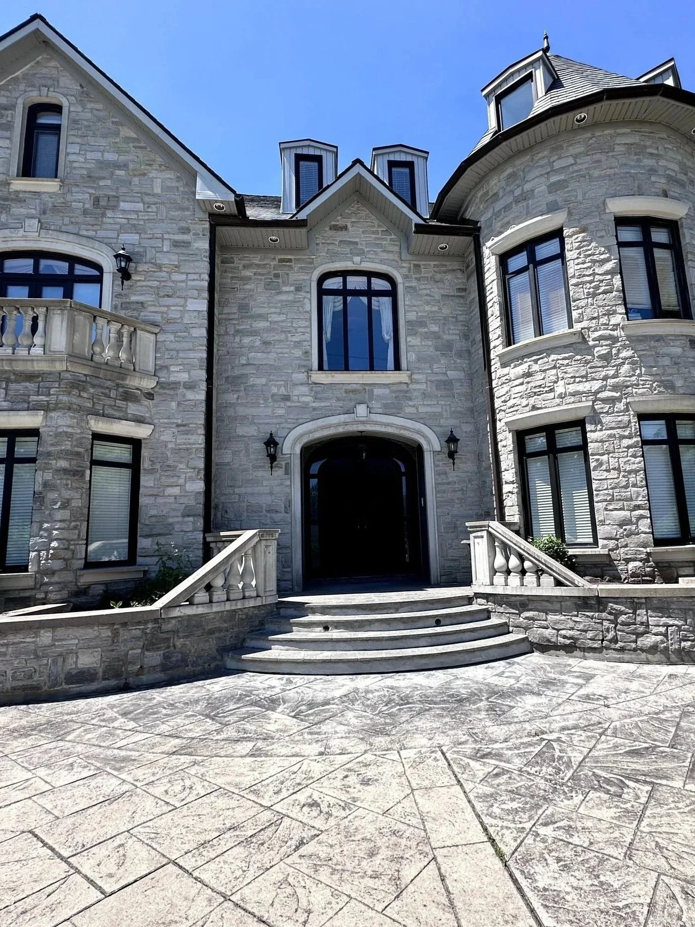 Front view of a large stone mansion with arched windows, a staircase leading up to the entrance, and a clear blue sky above.