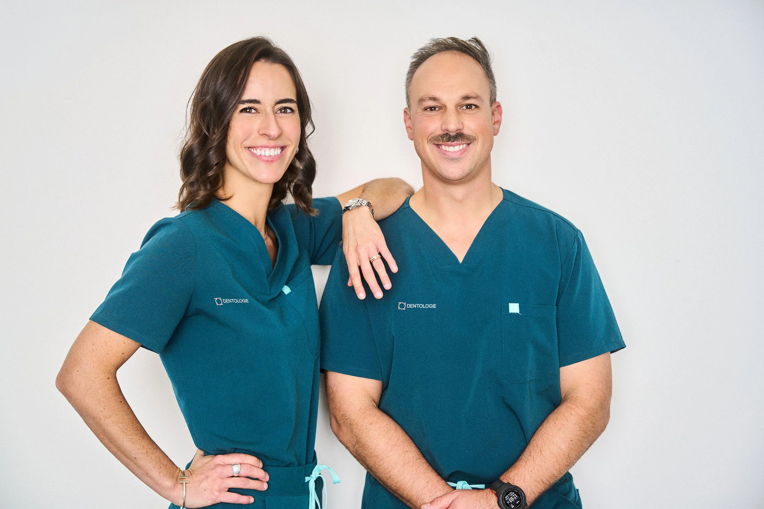 Deux professionnels de la dentisterie souriants en blouse médicale bleue, posant côte à côte.