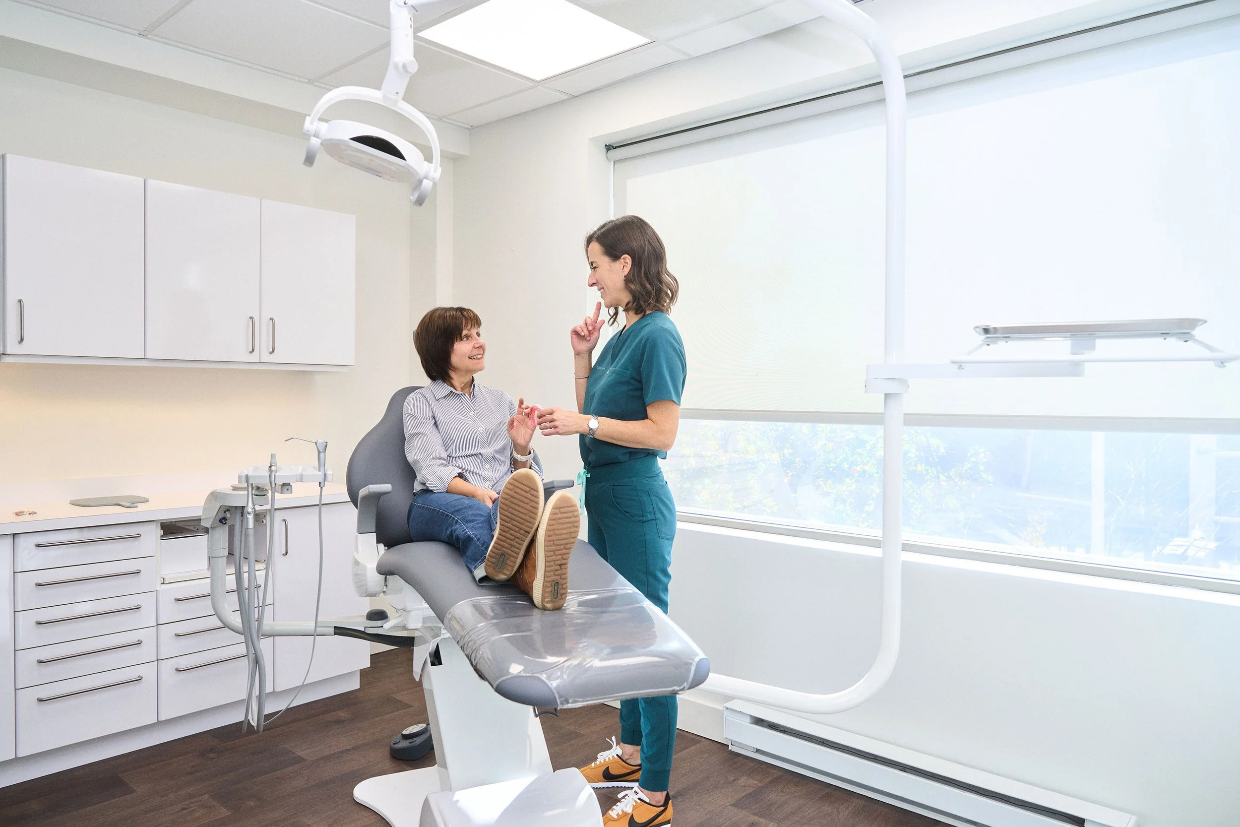 Patiente installée dans un fauteuil dentaire, discutant avec une dentiste dans un cabinet moderne.